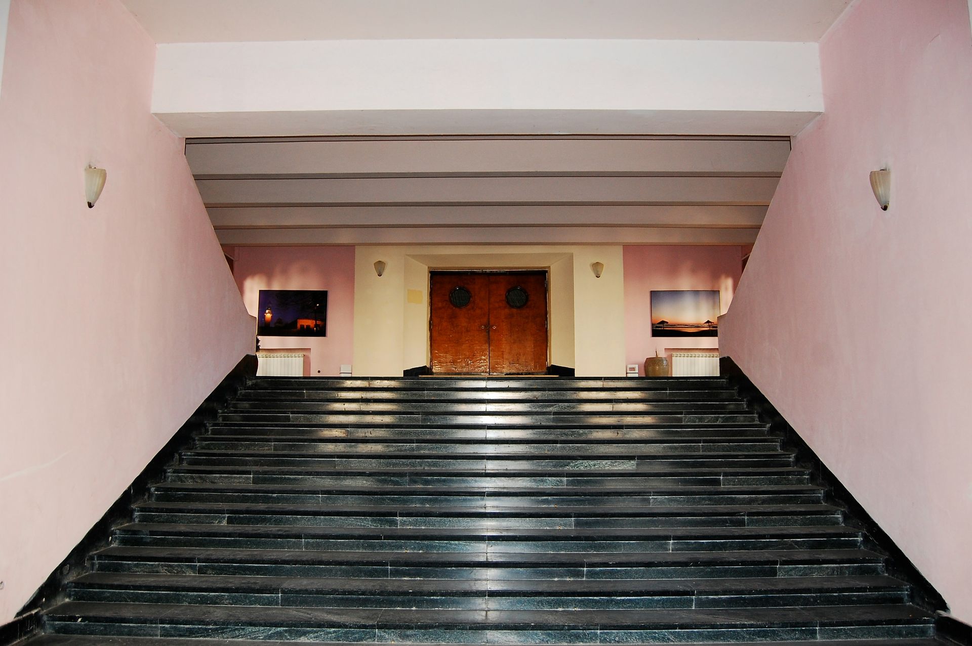 A wide staircase of black stone leads up to wooden double doors, pink walls and a white ceiling.
