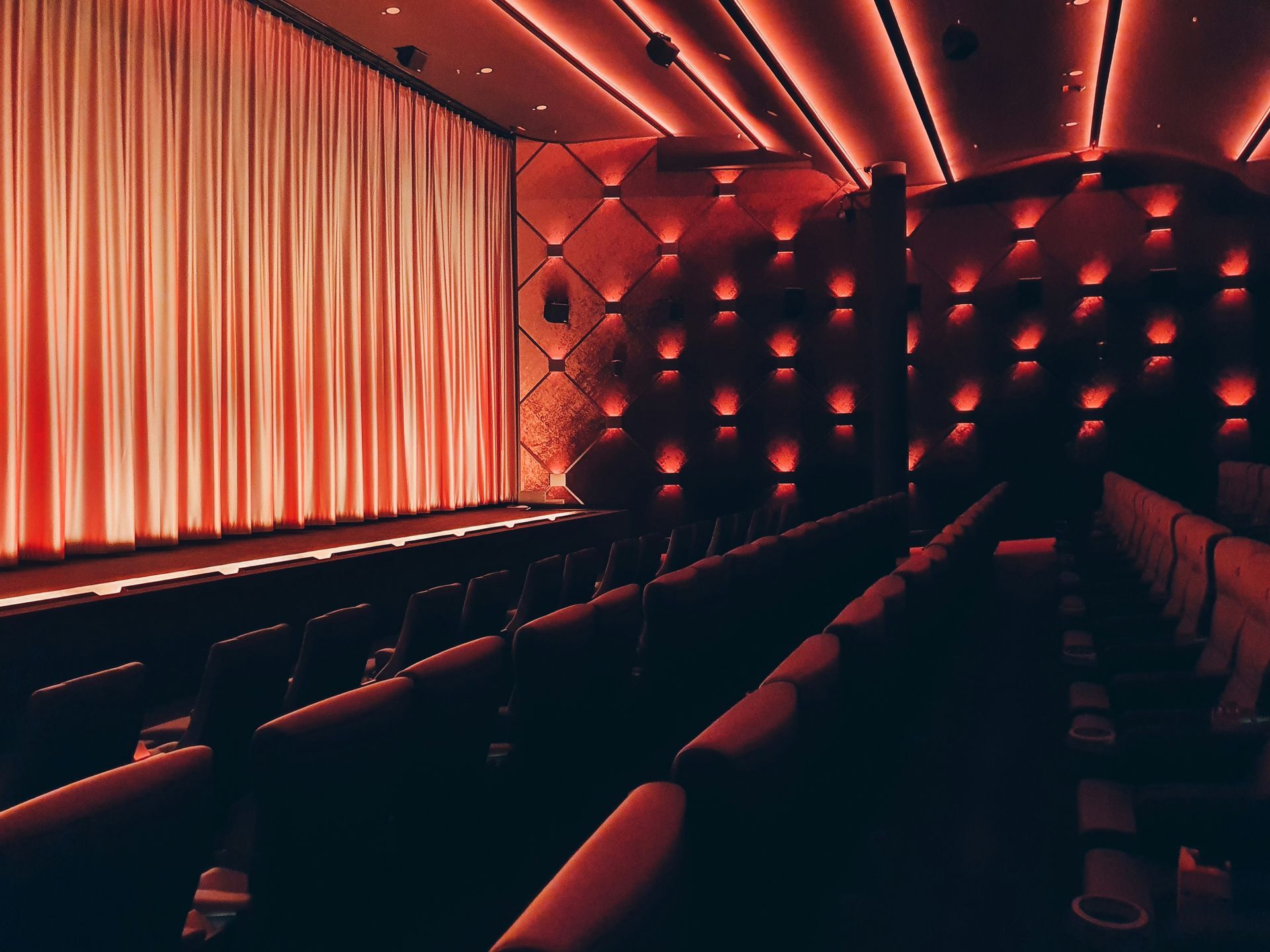Empty red-lit movie theater with rows of seats facing a large curtain.