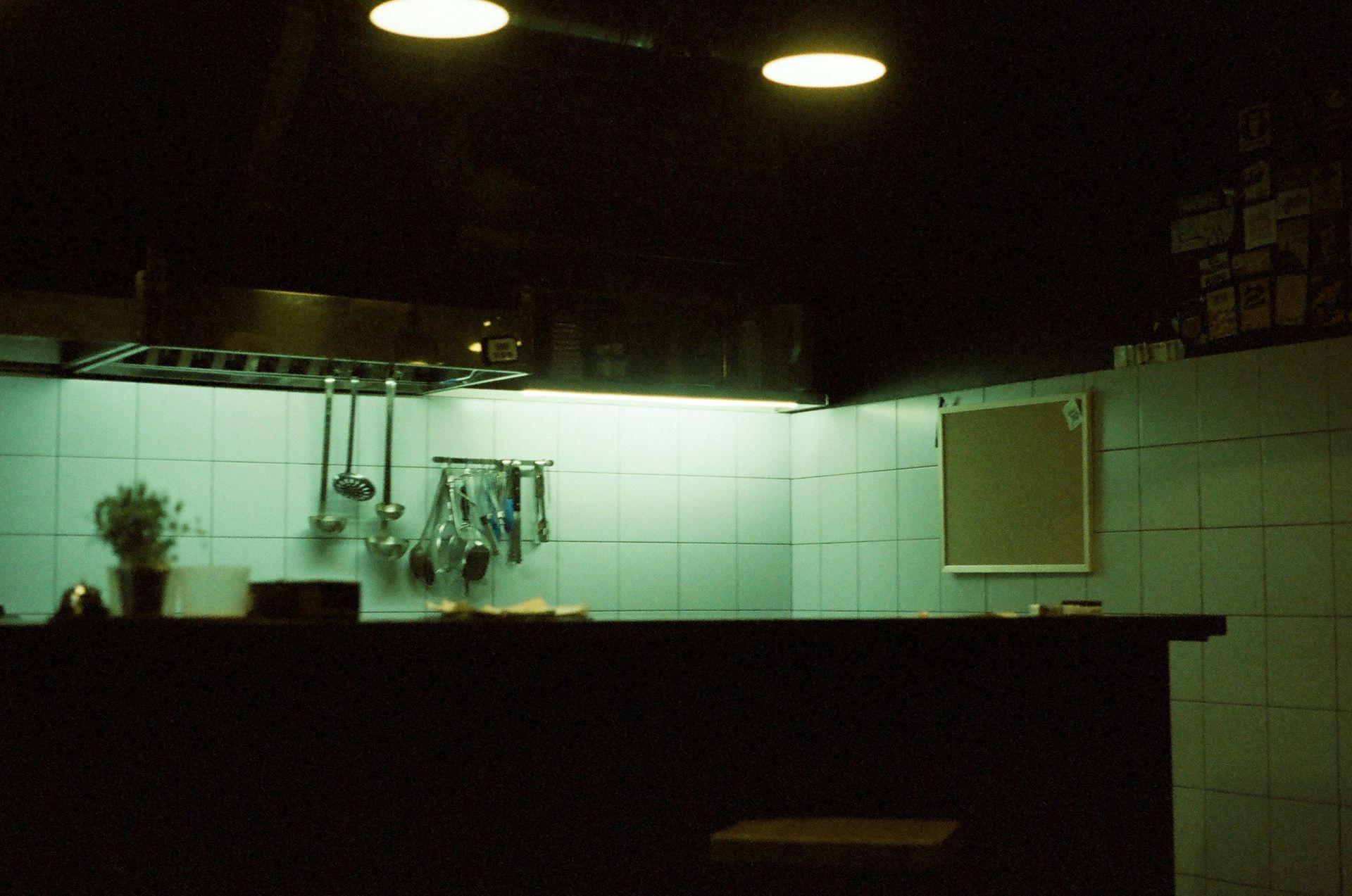 Dark kitchen corner with overhead lights, tiled walls, and hanging utensils.