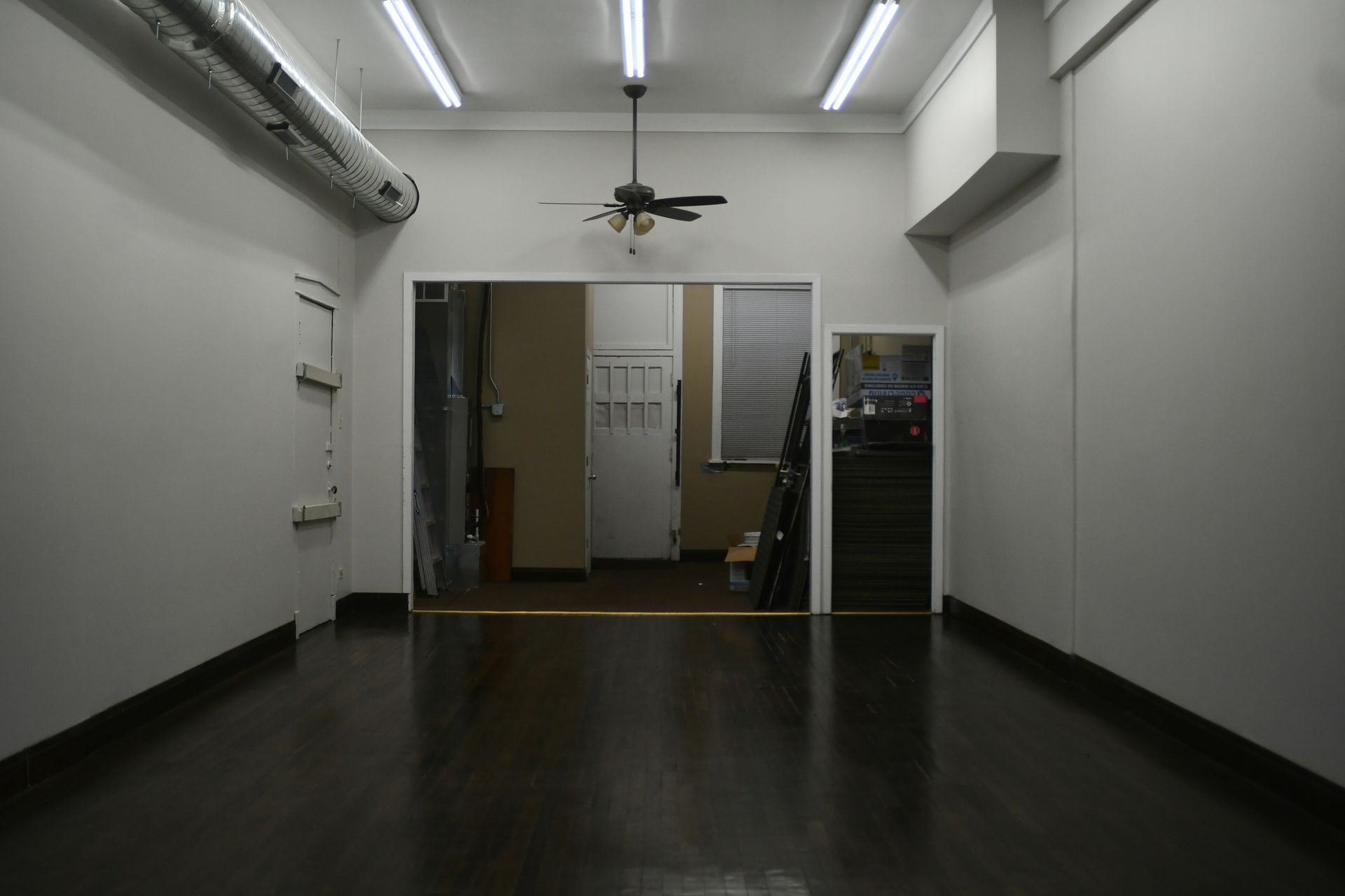 Empty room with dark hardwood floors, white walls, and a doorway leading to other rooms.