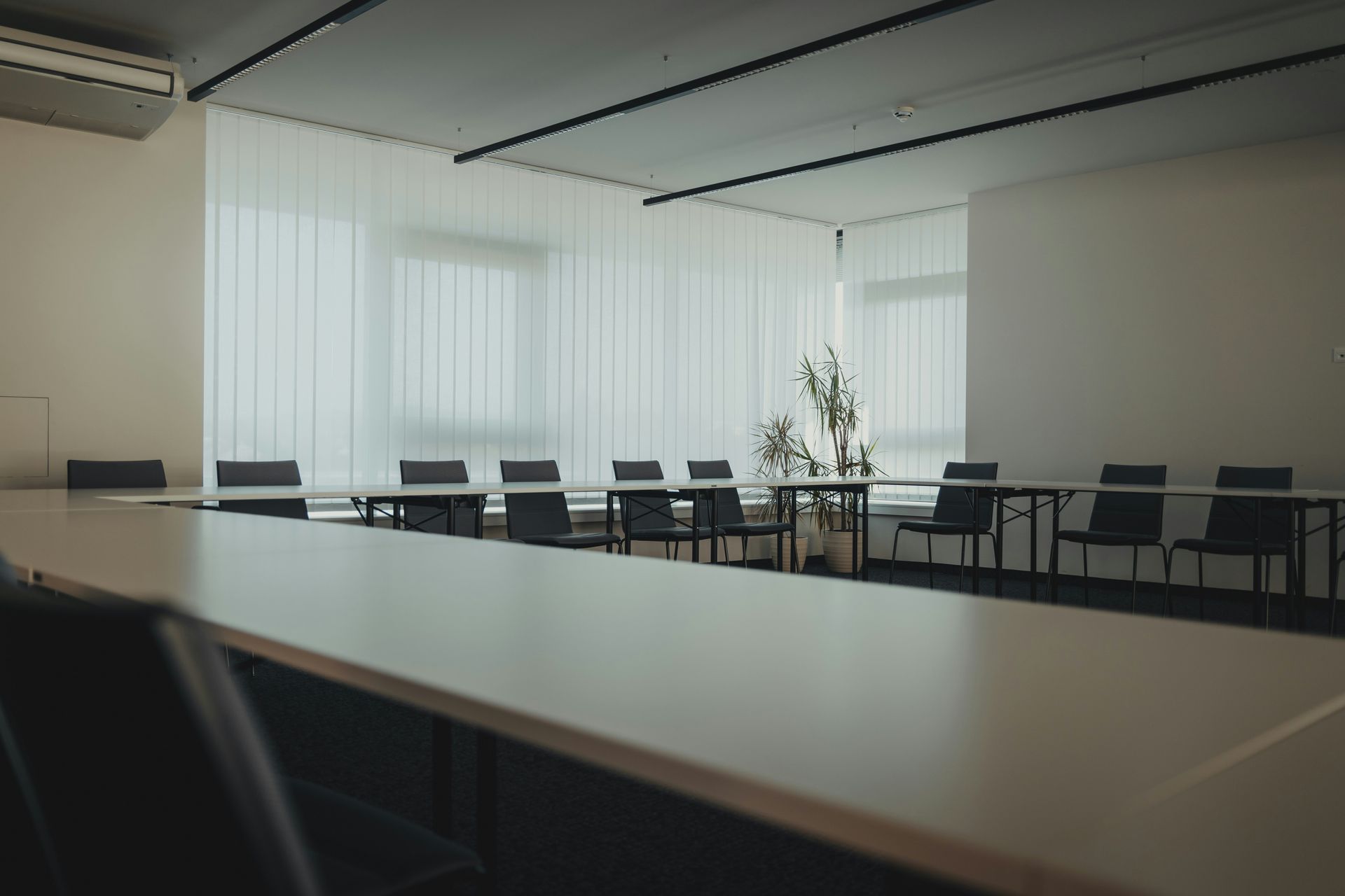 Empty conference room with a long table, chairs, and a window with white curtains.