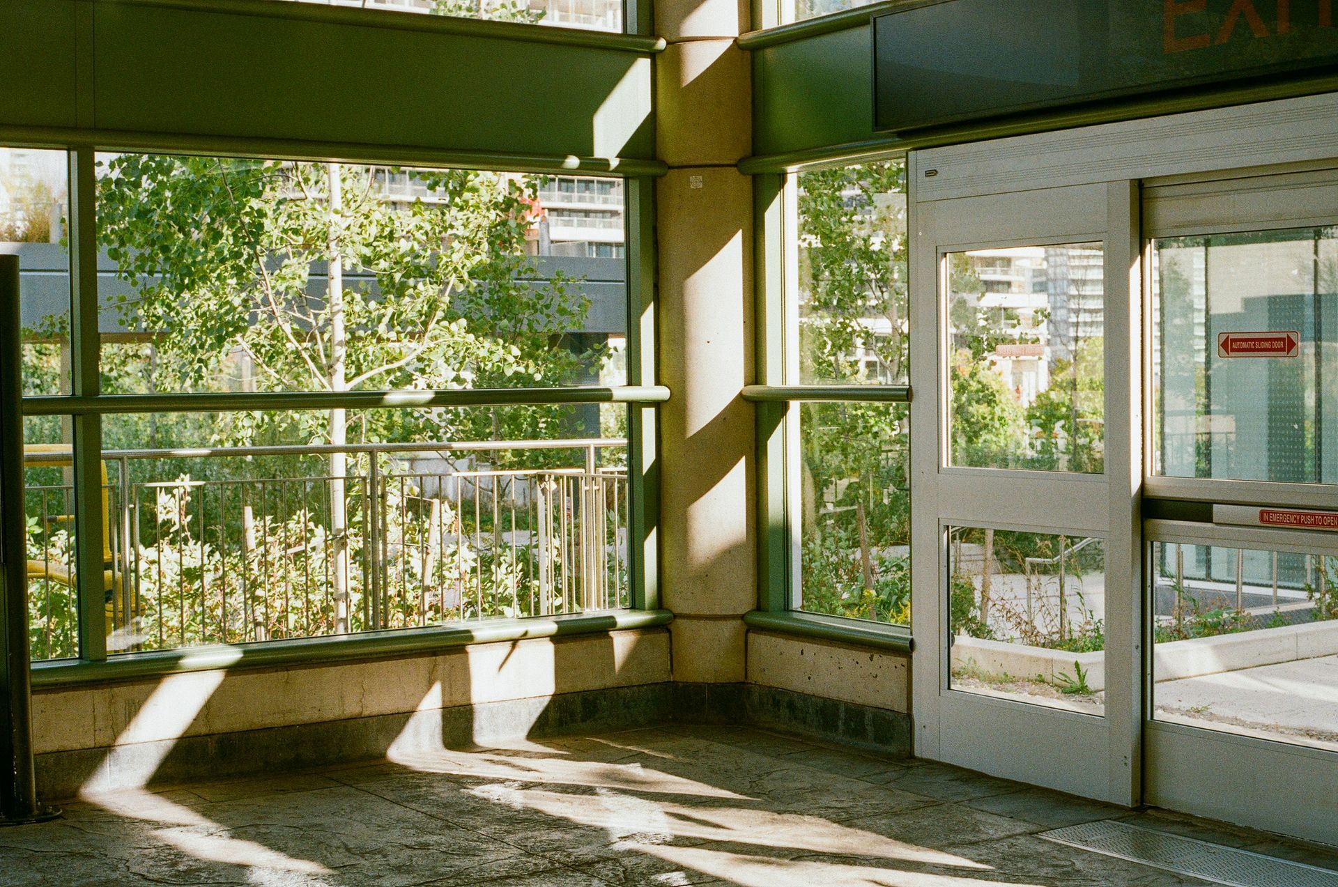 Indoor corner with windows overlooking trees; doorway on right, sunlight casts shadows.