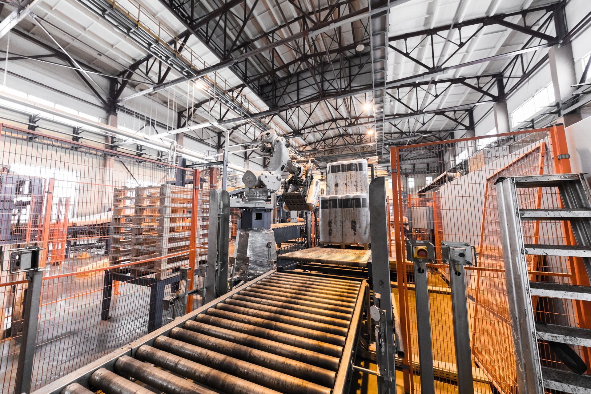 Industrial interior: conveyor belt, machinery, metal structure, and pallets in a factory setting.