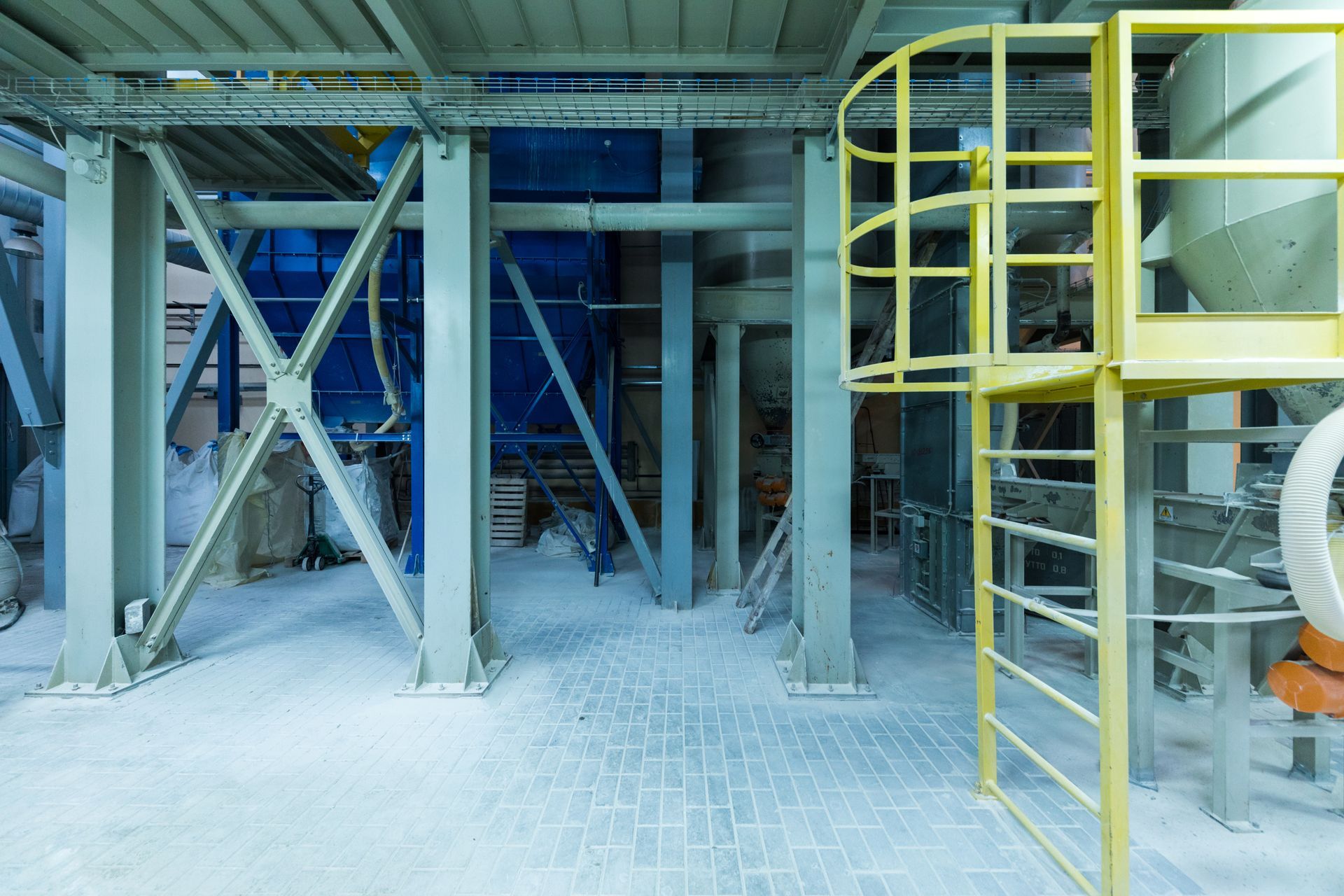 Interior of a factory with machinery, steel beams, and a yellow safety ladder, covered in a white powder.