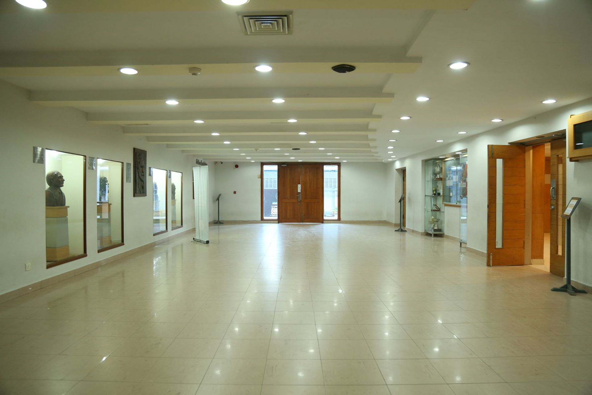 Empty museum hallway with light-colored walls and floor, glass display cases, and a large wooden door.