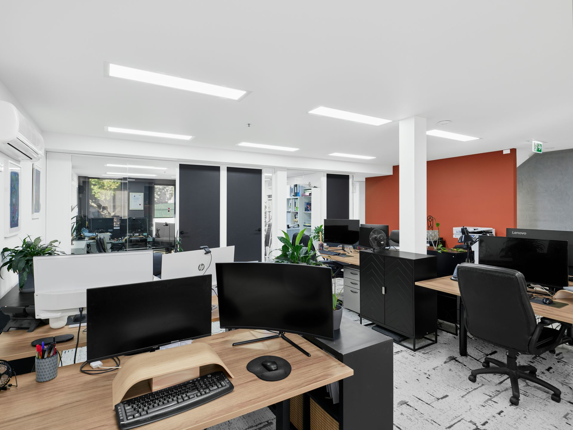 Open office space with desks, computers, and office chairs. A large window is in the background.