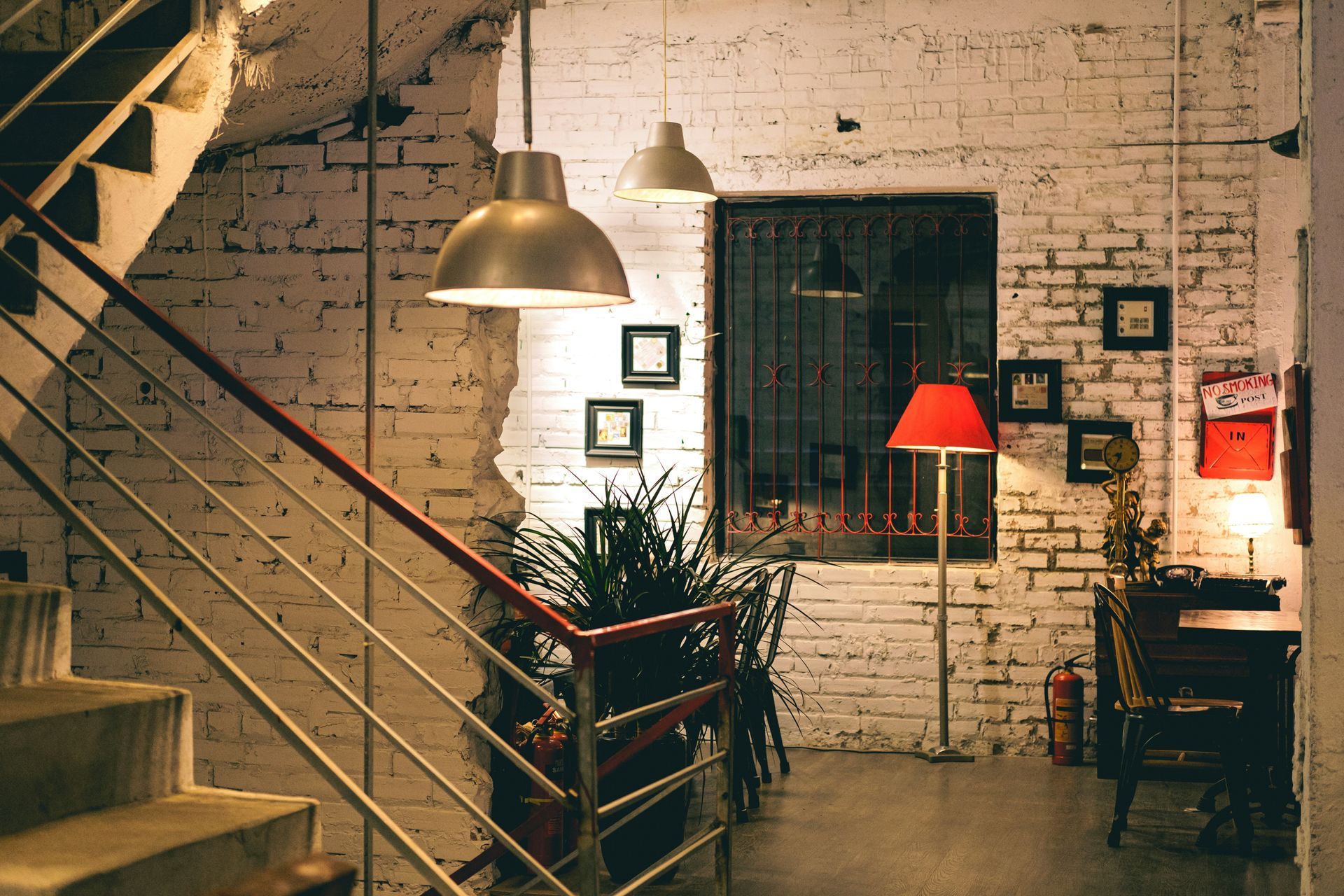 Staircase leads to a cozy room with exposed brick walls, metal railing, and hanging lights.