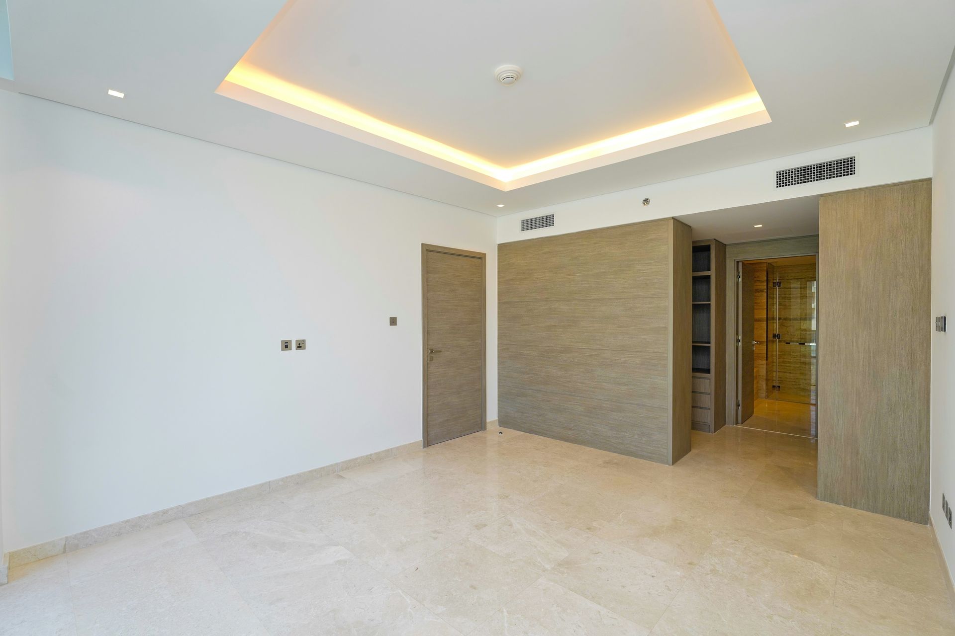 Empty modern bedroom with beige walls, marble floor, and recessed ceiling lighting.