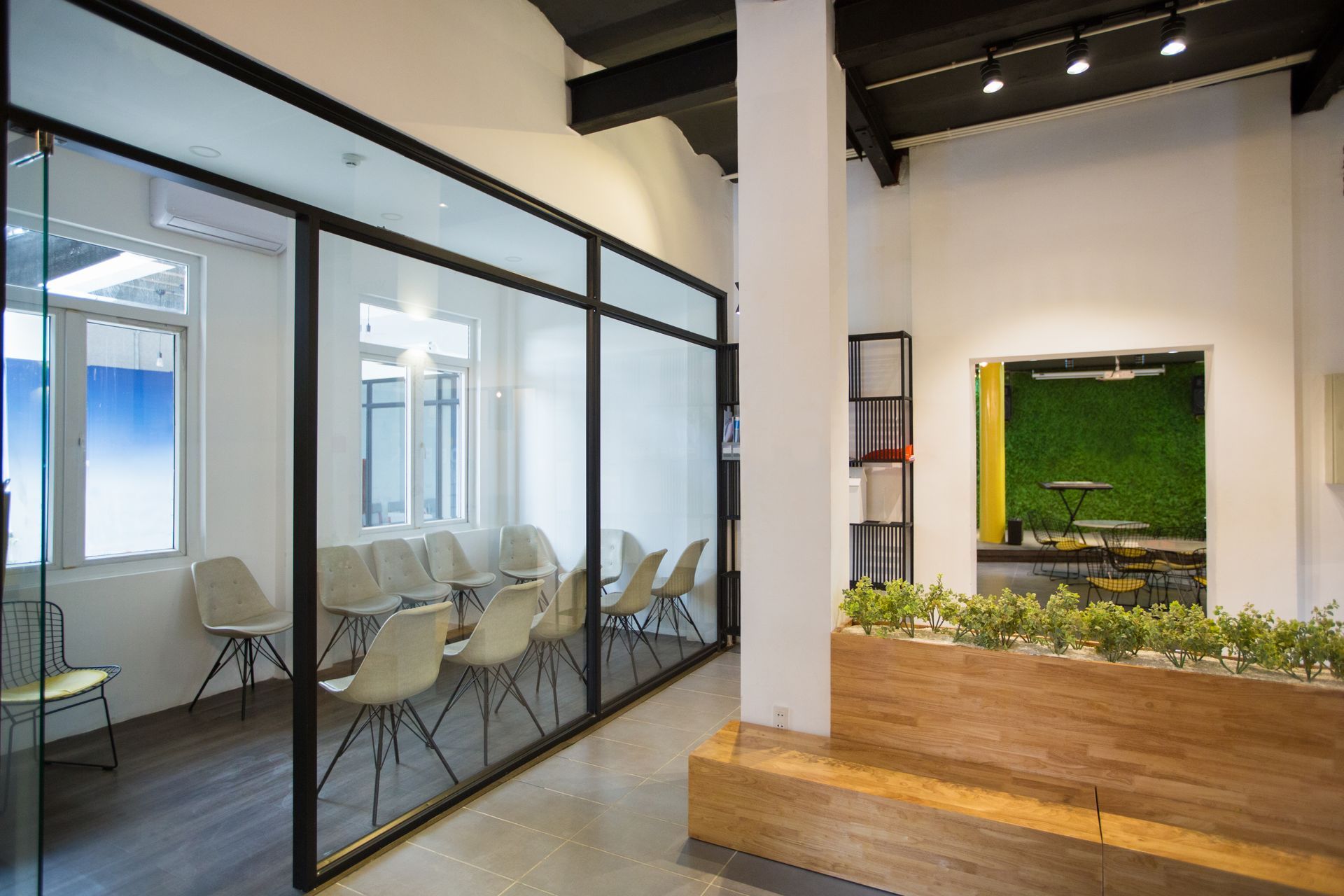 Interior office with glass walls, chairs, and a green wall, with a wooden bench and planters.