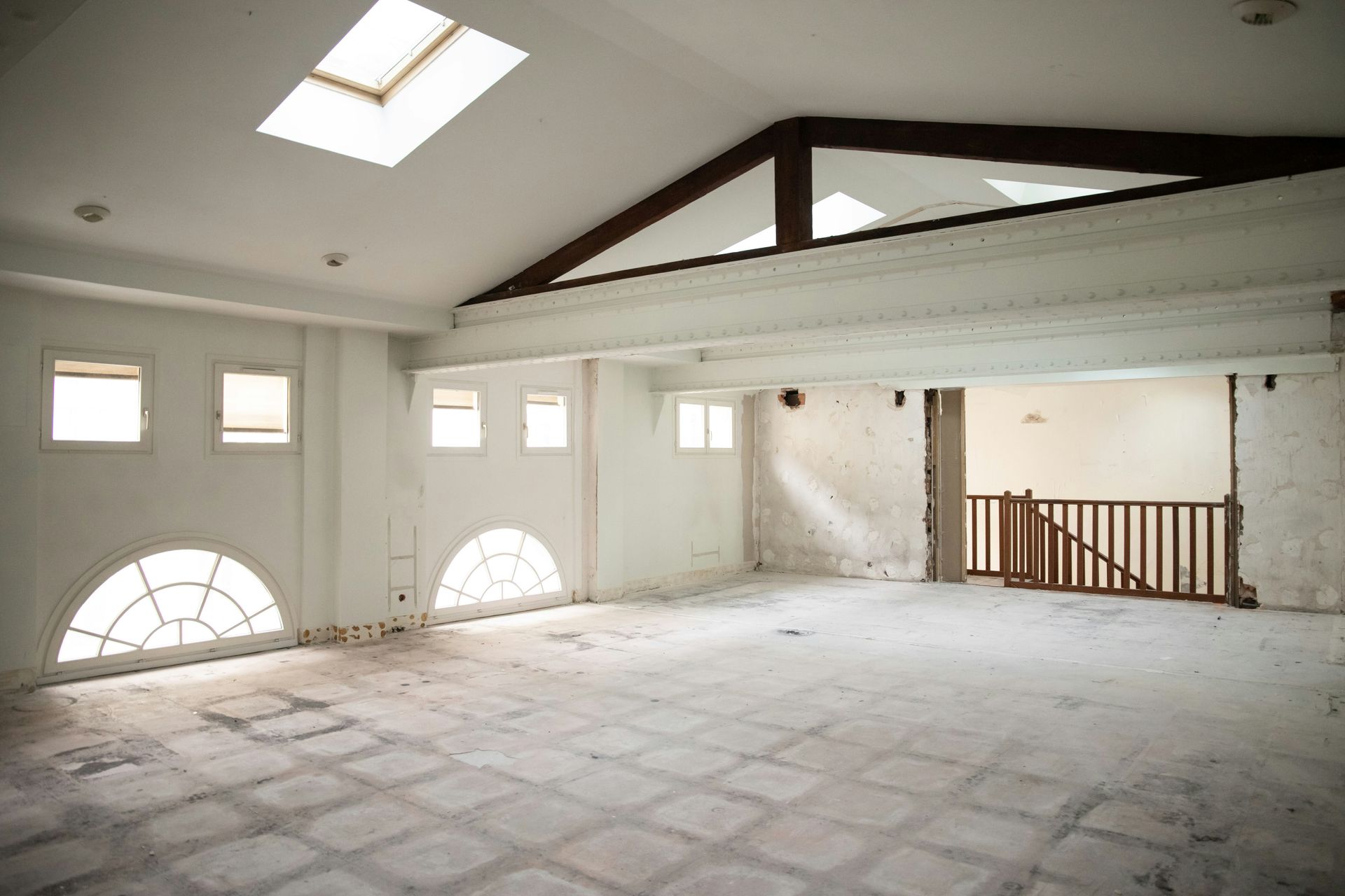 Empty, spacious room with arched windows, skylight, and exposed beams.