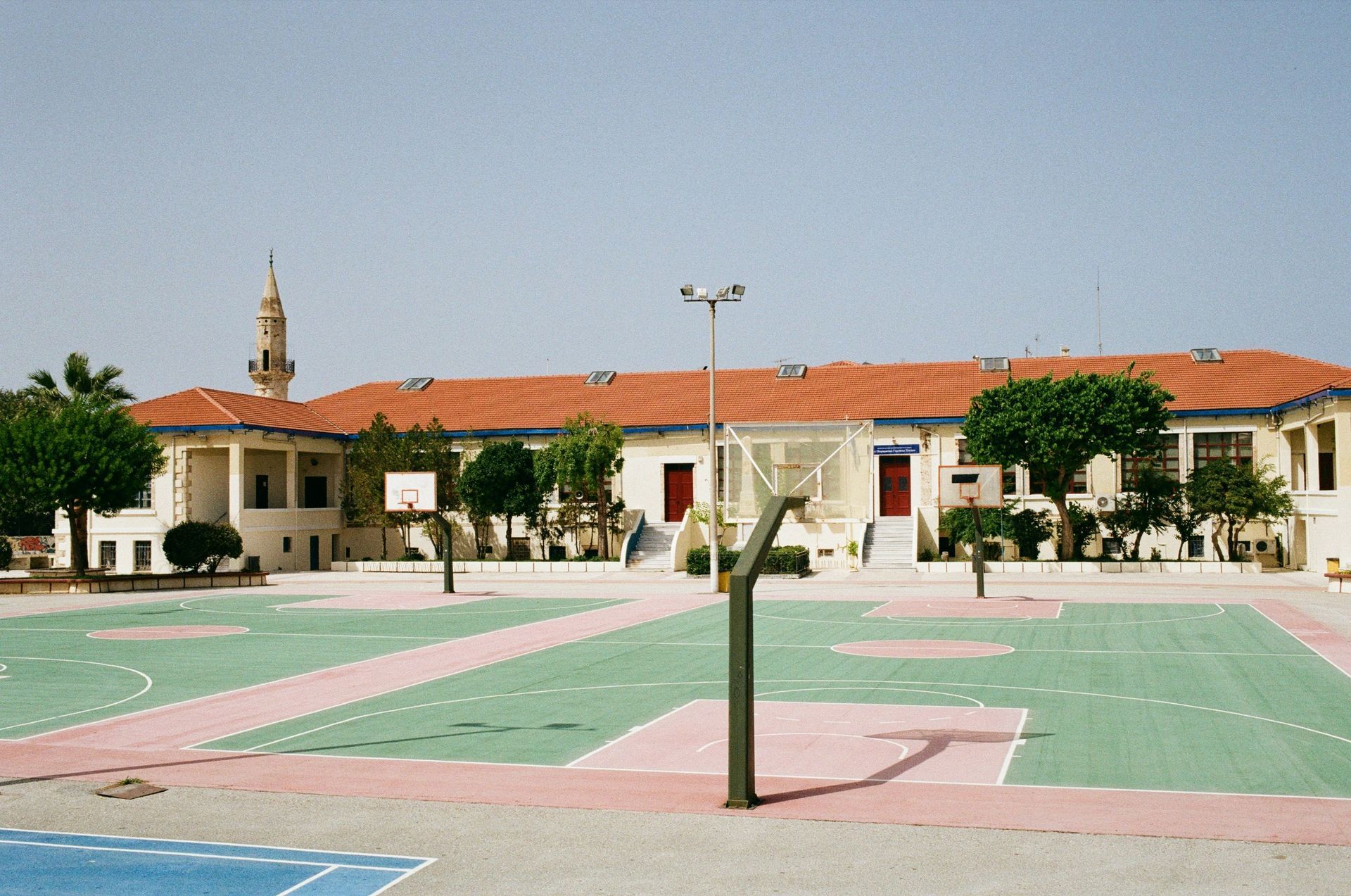 School courtyard with basketball courts and a building featuring a minaret in the background.