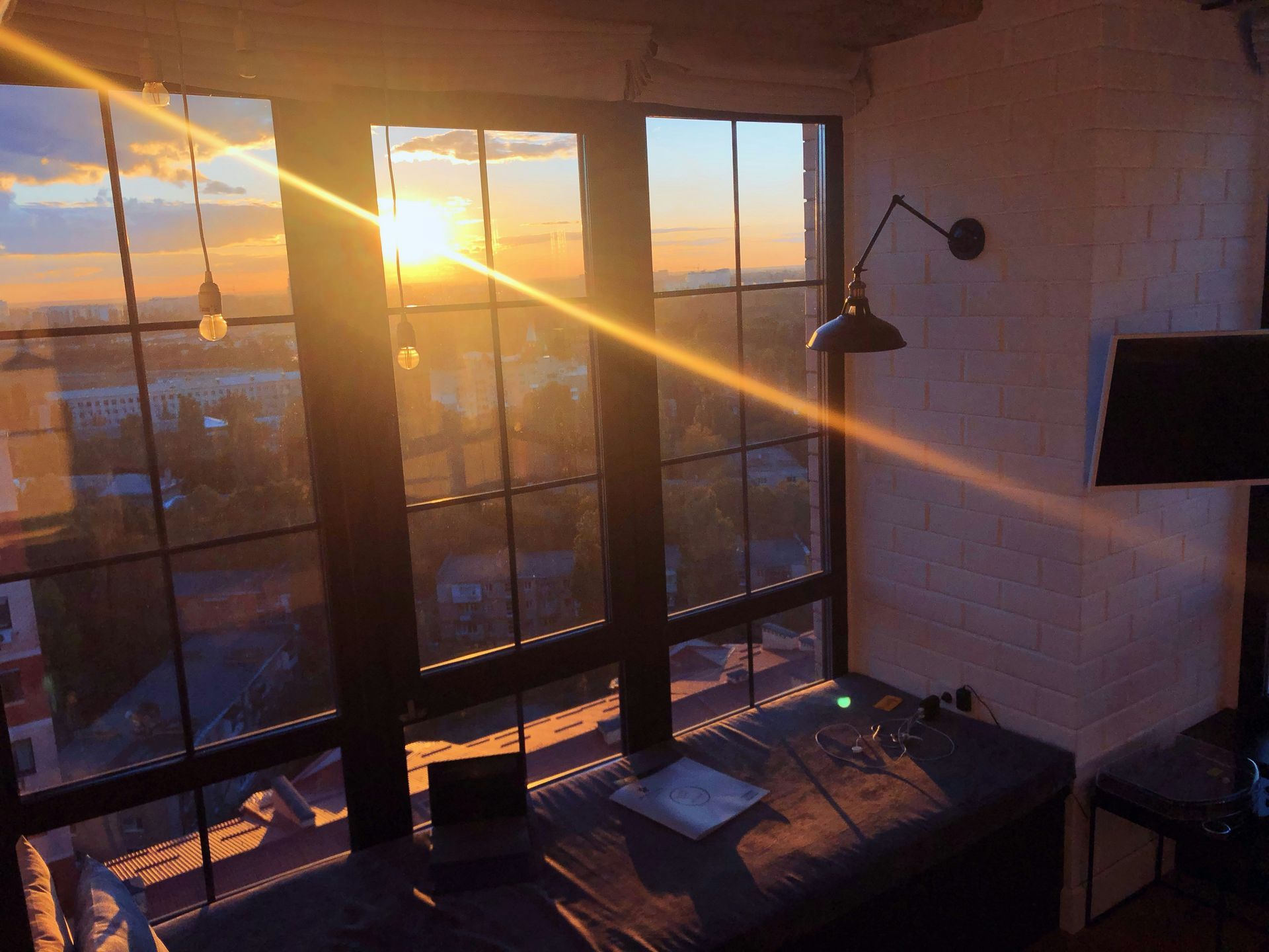 Sunset view through large windows, illuminating a workspace with laptop and desk lamp.