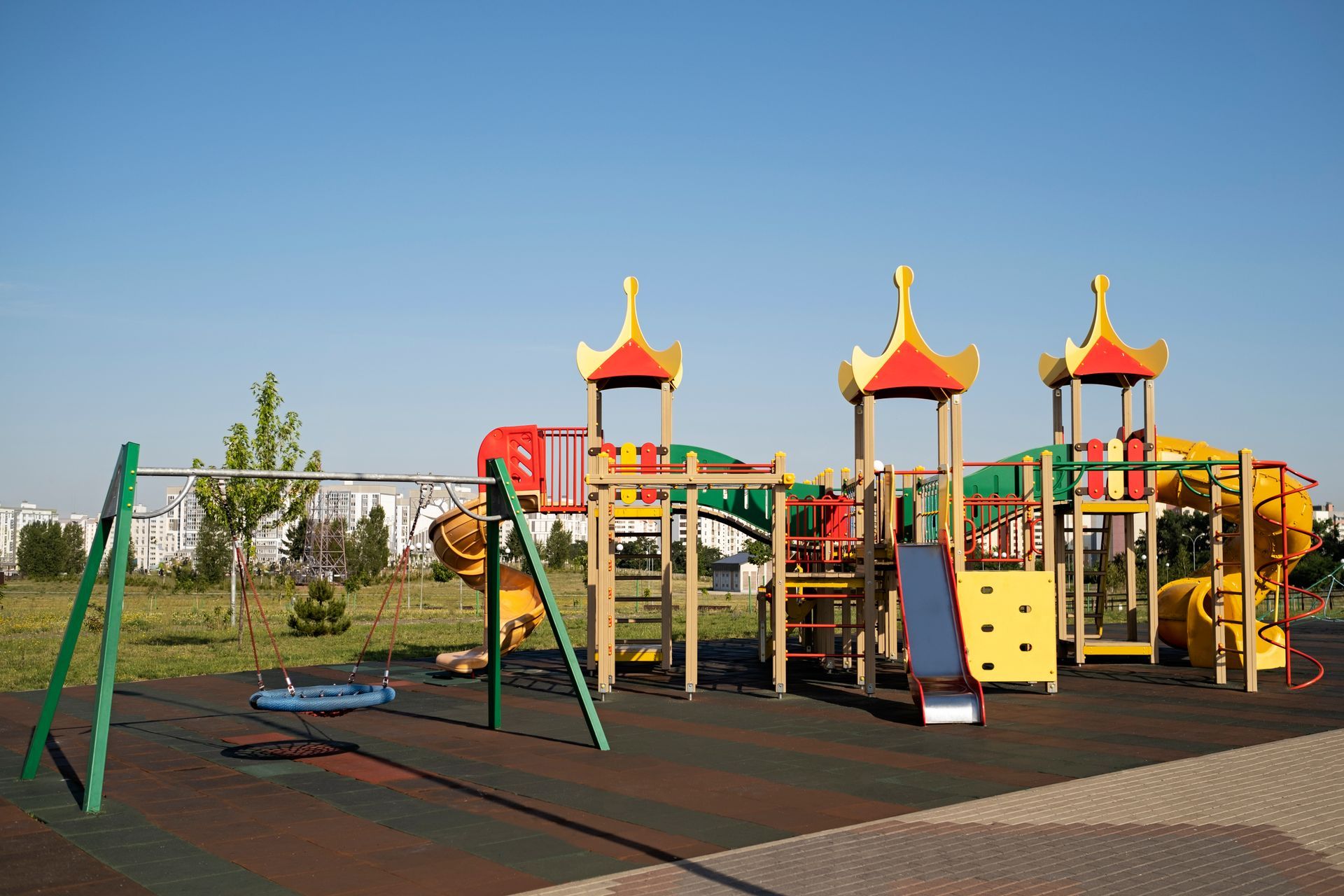 Empty playground with swings and colorful climbing structures under a clear blue sky.