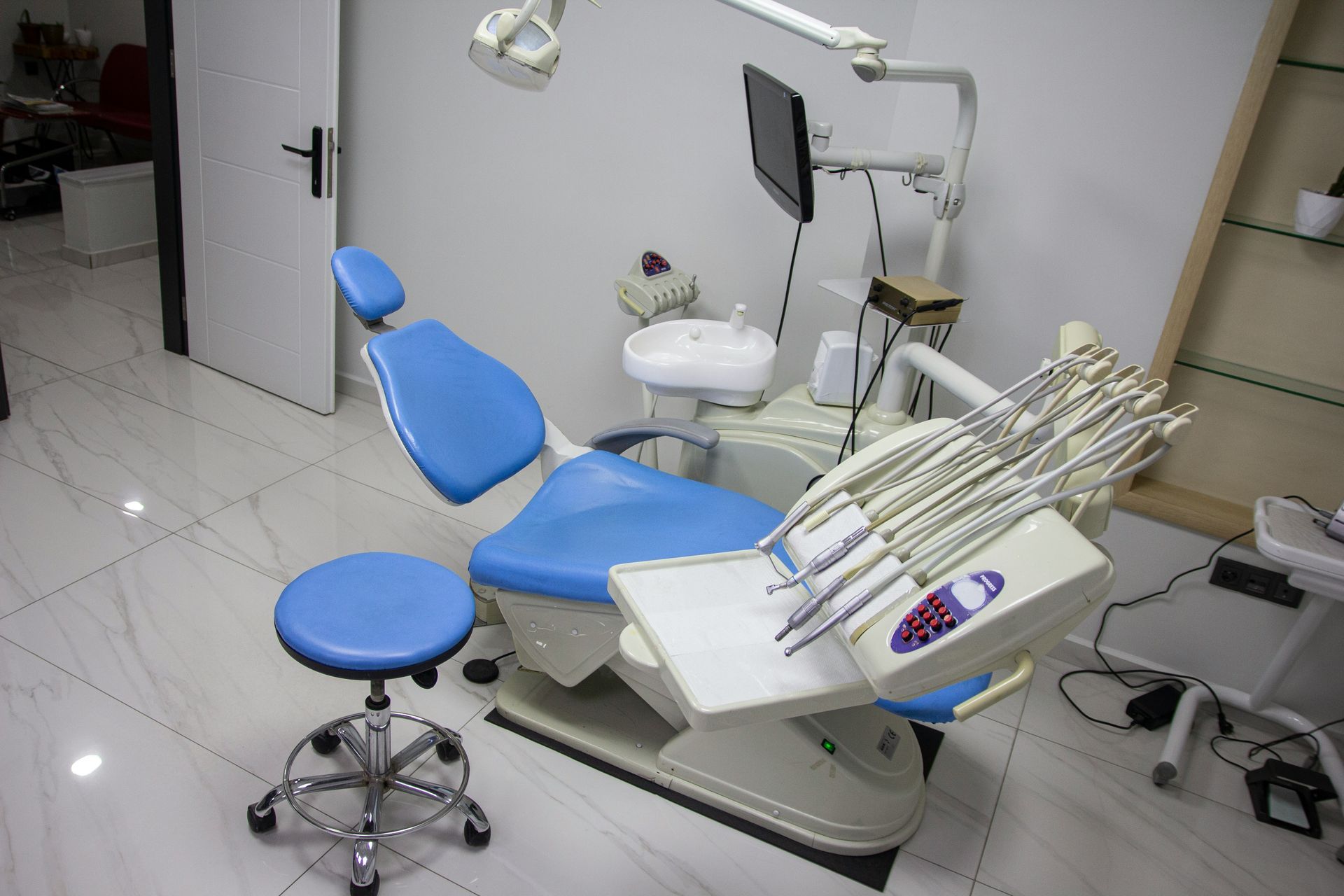 Blue dental chair and stool in a white-walled room, with dental tools and equipment.
