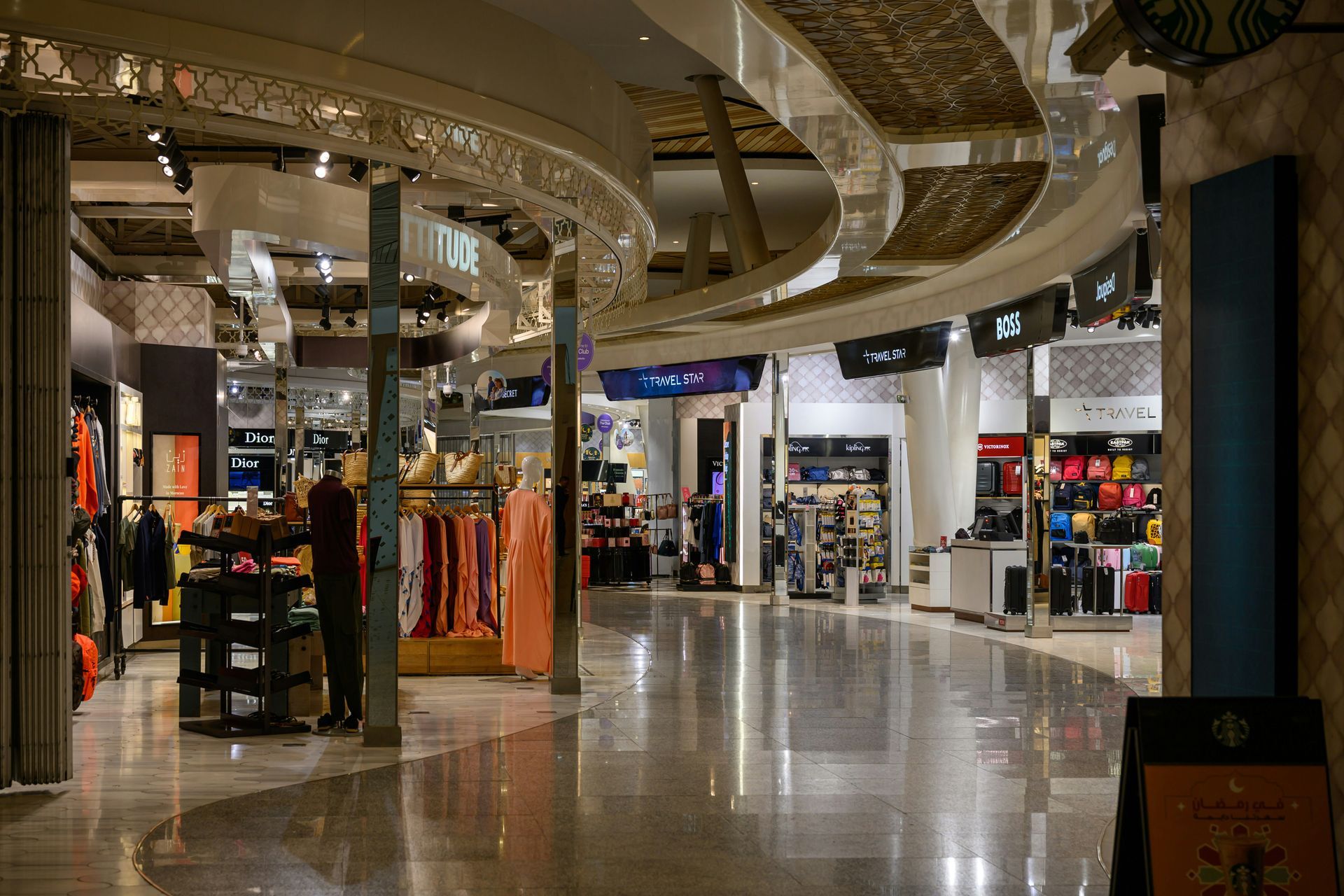 Interior view of a shopping mall with stores along a curved corridor. Gold-colored ornate ceiling and polished floor.