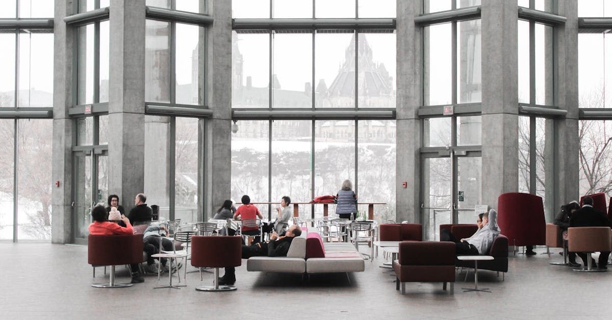 People sit in modern lobby with large windows overlooking a snowy landscape. Red and gray furniture.