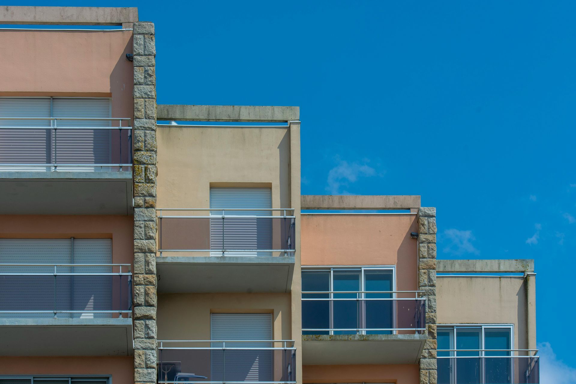 Apartment building with stepped design; balconies, peach-colored walls, blue sky.