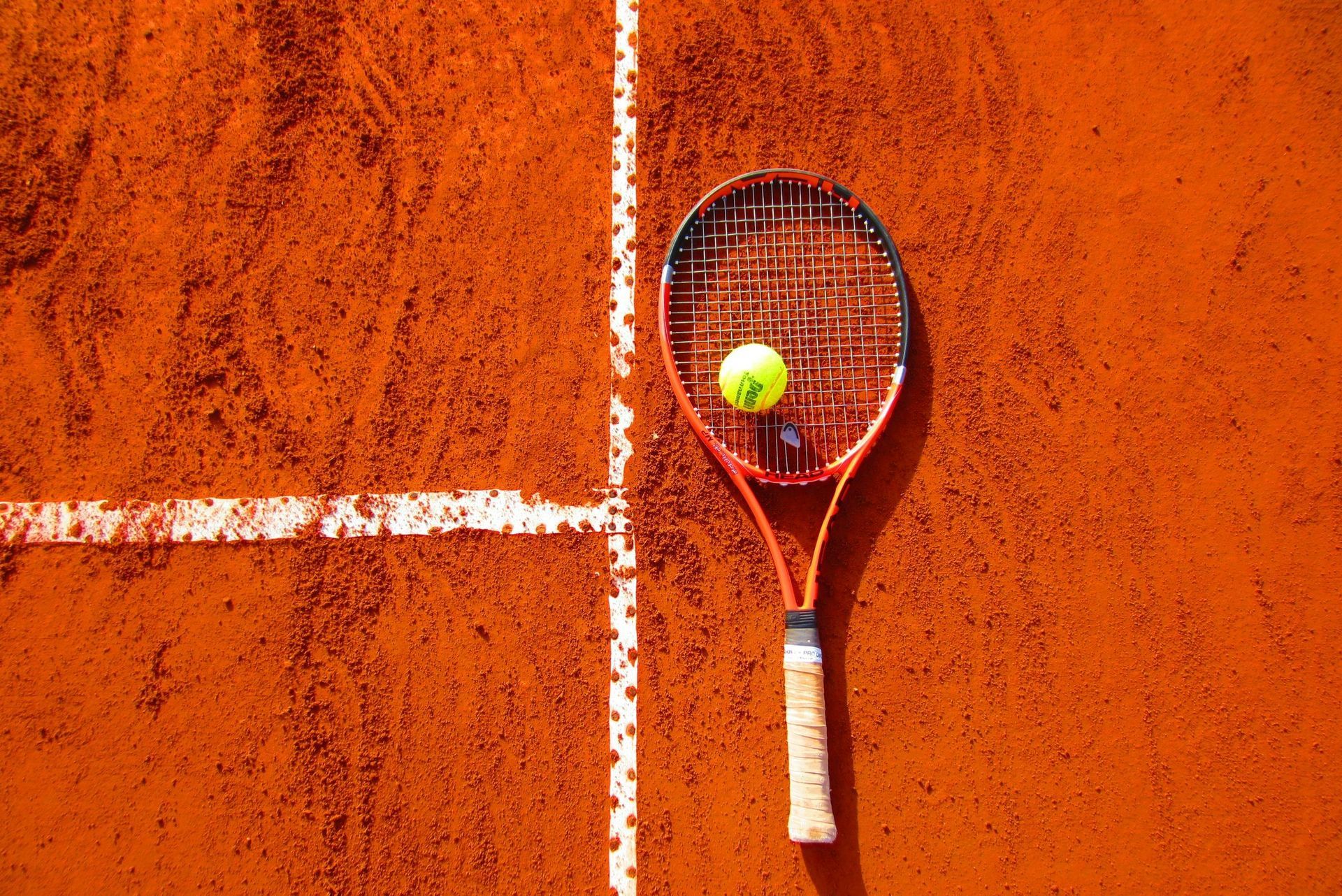 Tennis racket and ball on a clay court near a white line.