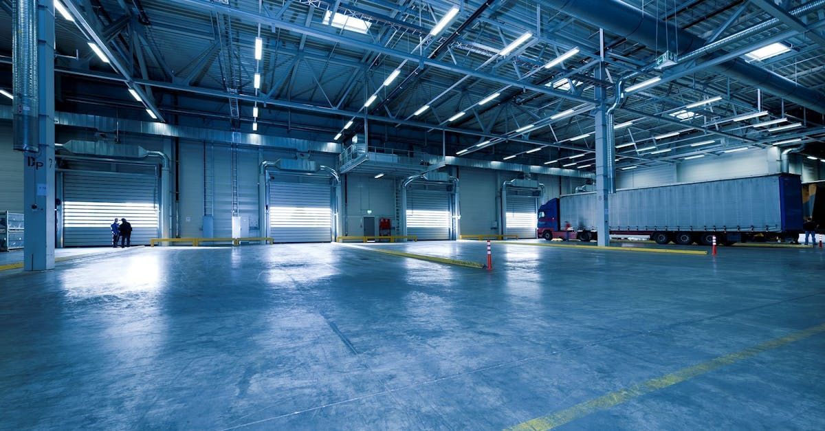 Large warehouse interior with loading docks, truck, and concrete floor, lit by overhead lights.