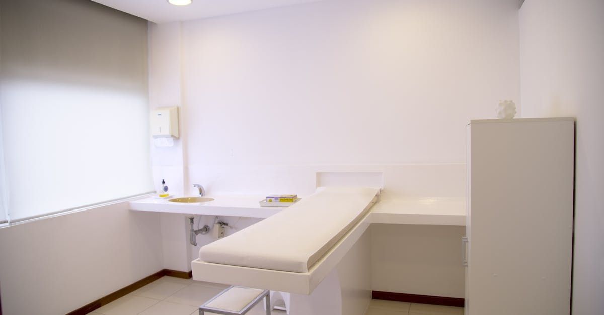 Clean, white-walled doctor's examination room with a medical bed and built-in counter.