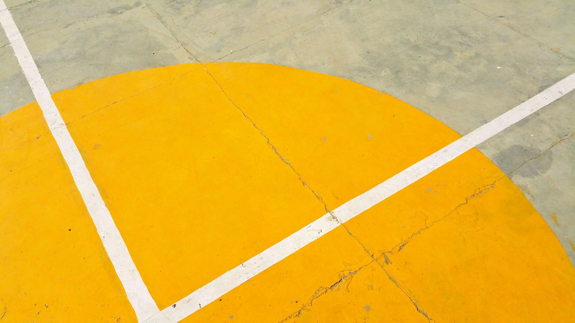 Yellow semicircle court marking with white lines on a concrete surface.