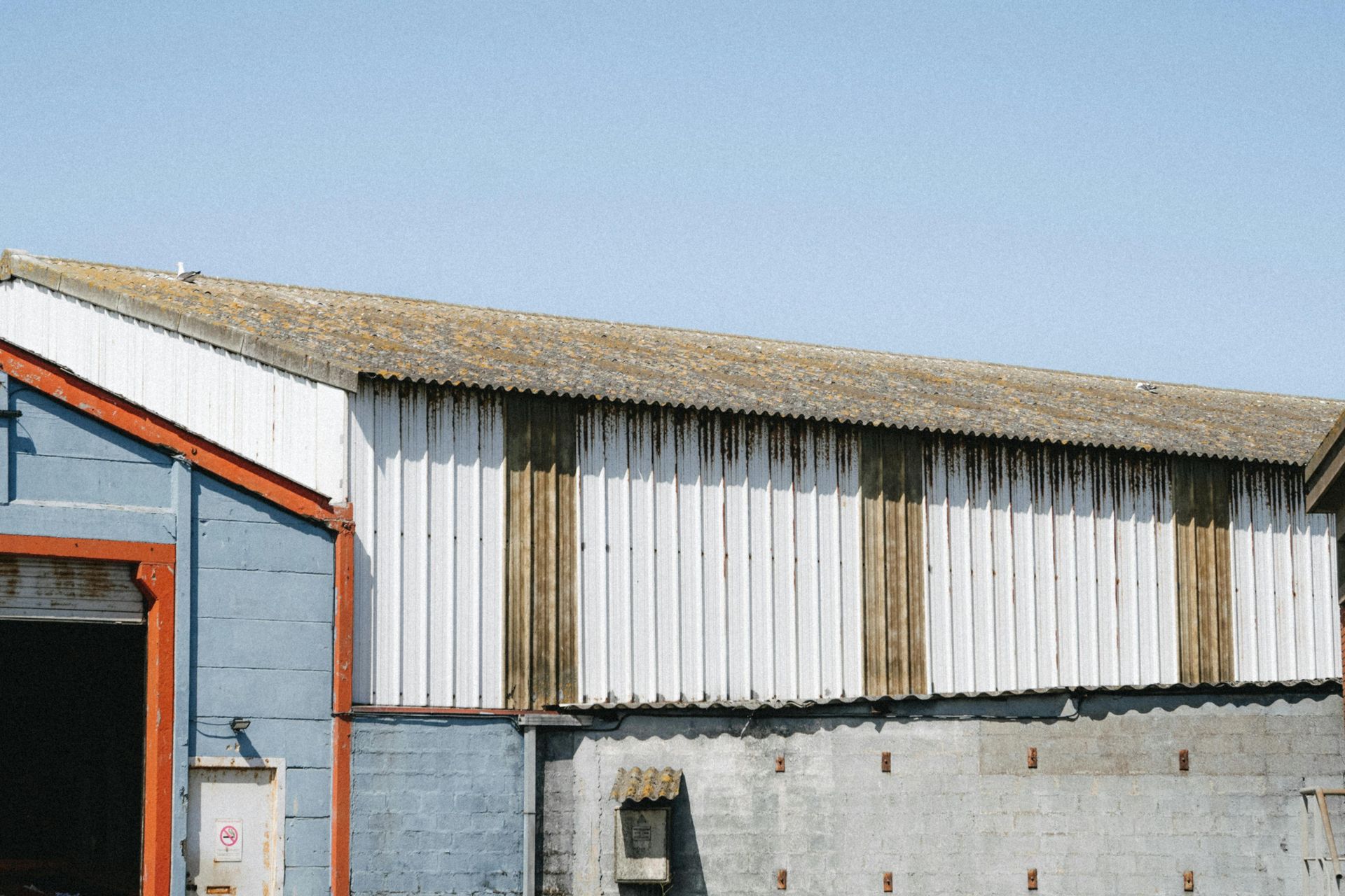 Barn with white and weathered siding, corrugated roof, and clear sky.