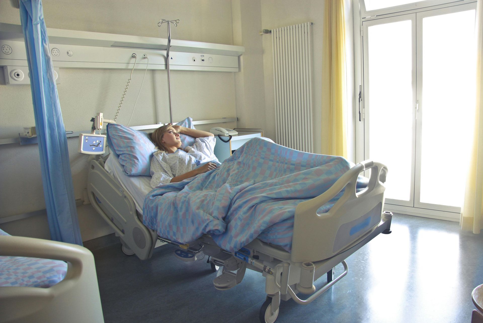 Person in hospital bed, blue sheets, window with bright light.