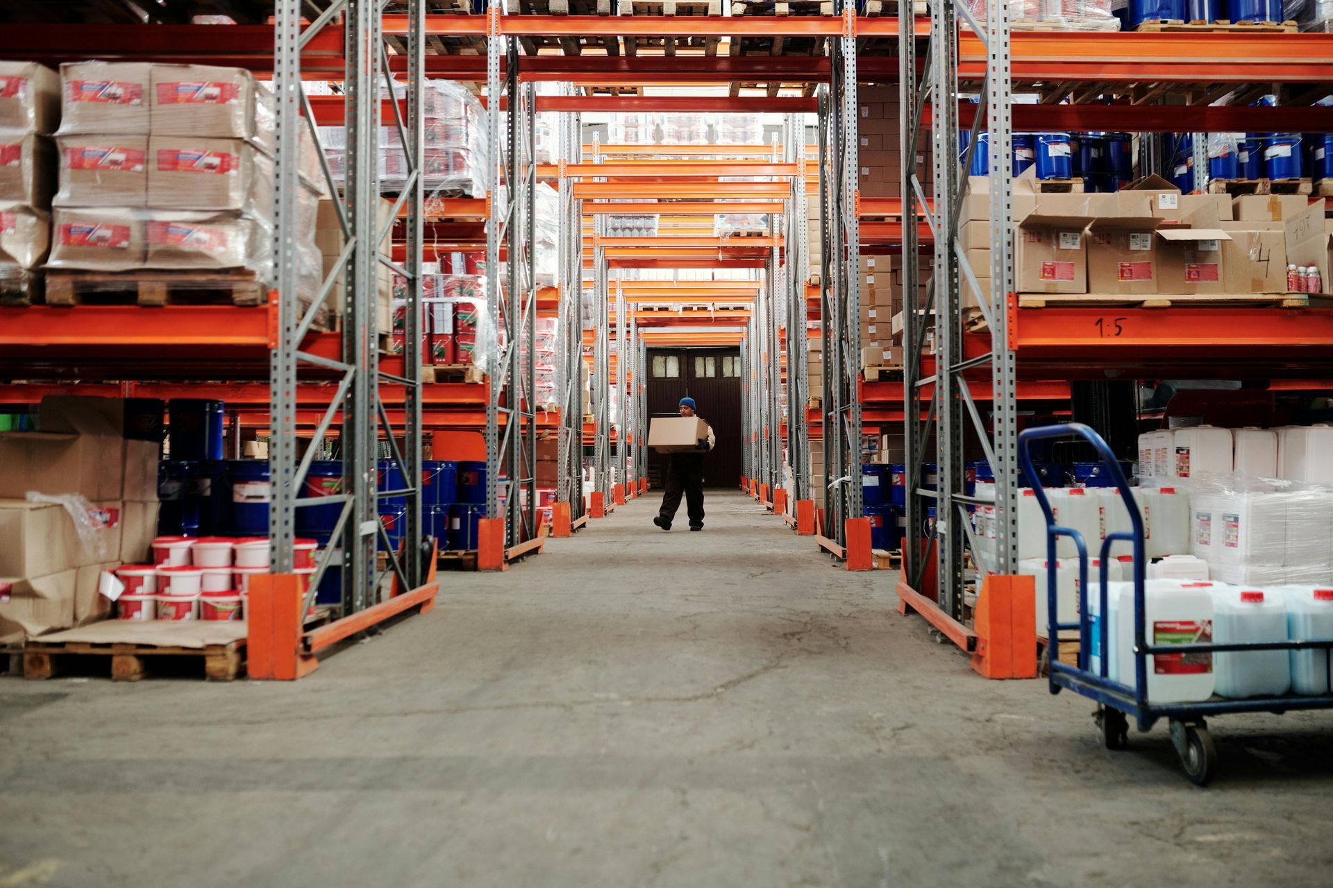 Two people in a warehouse packing orders. One places a box on a shelf, the other at a desk writing.