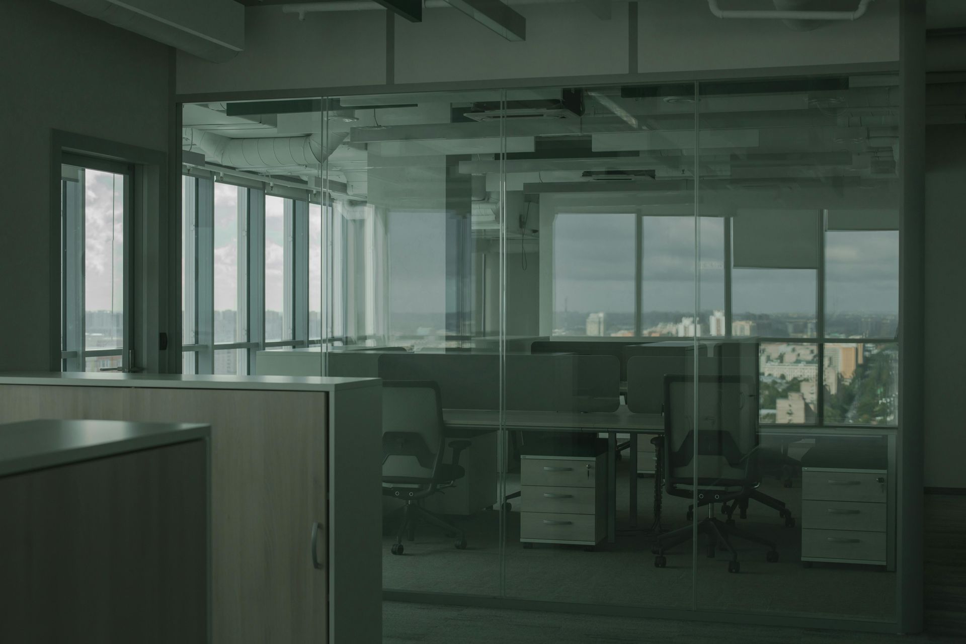 An empty modern office with glass walls, desks, and a city view outside the windows.