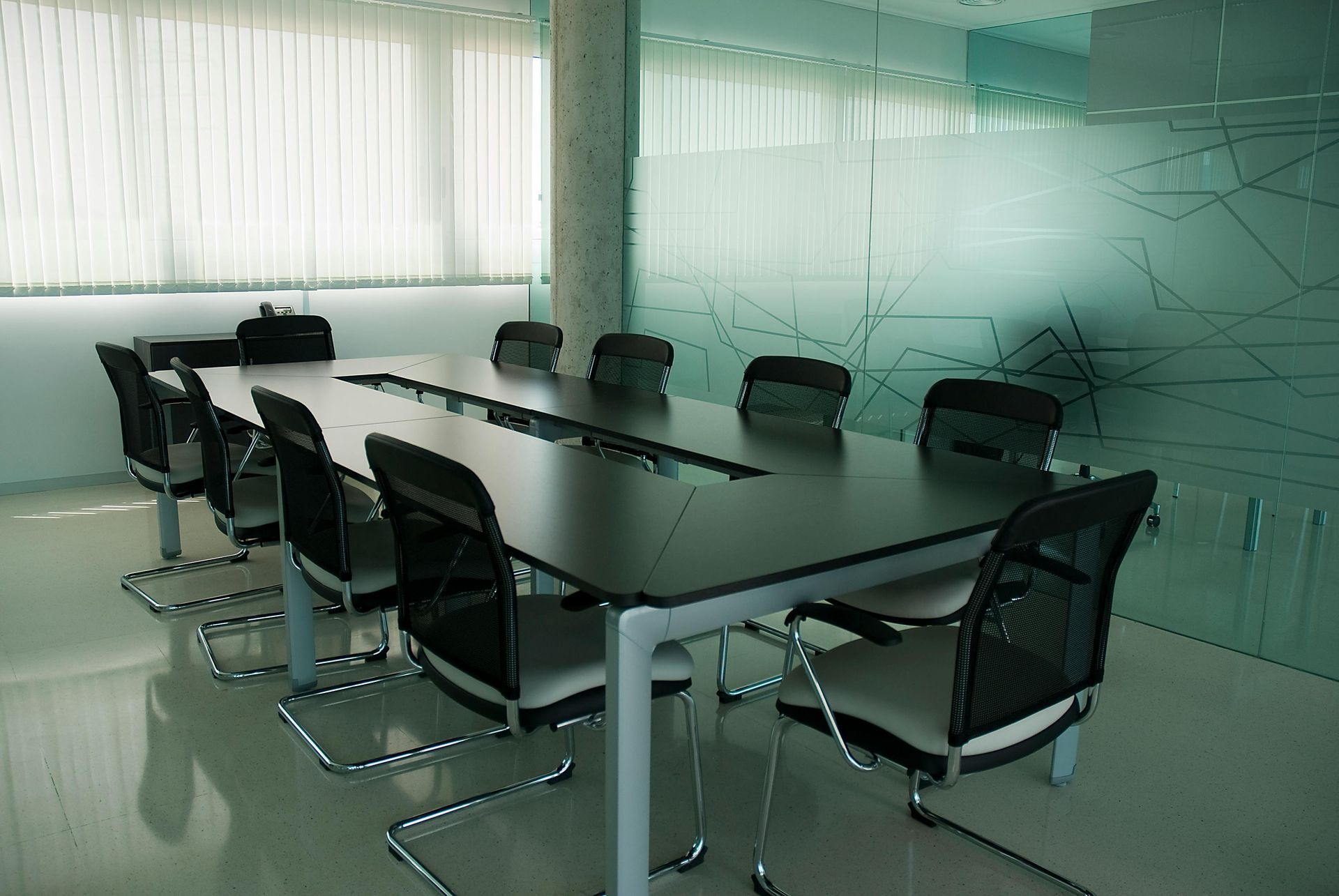 Conference room with long table and chairs. Frosted glass wall, large window with blinds.