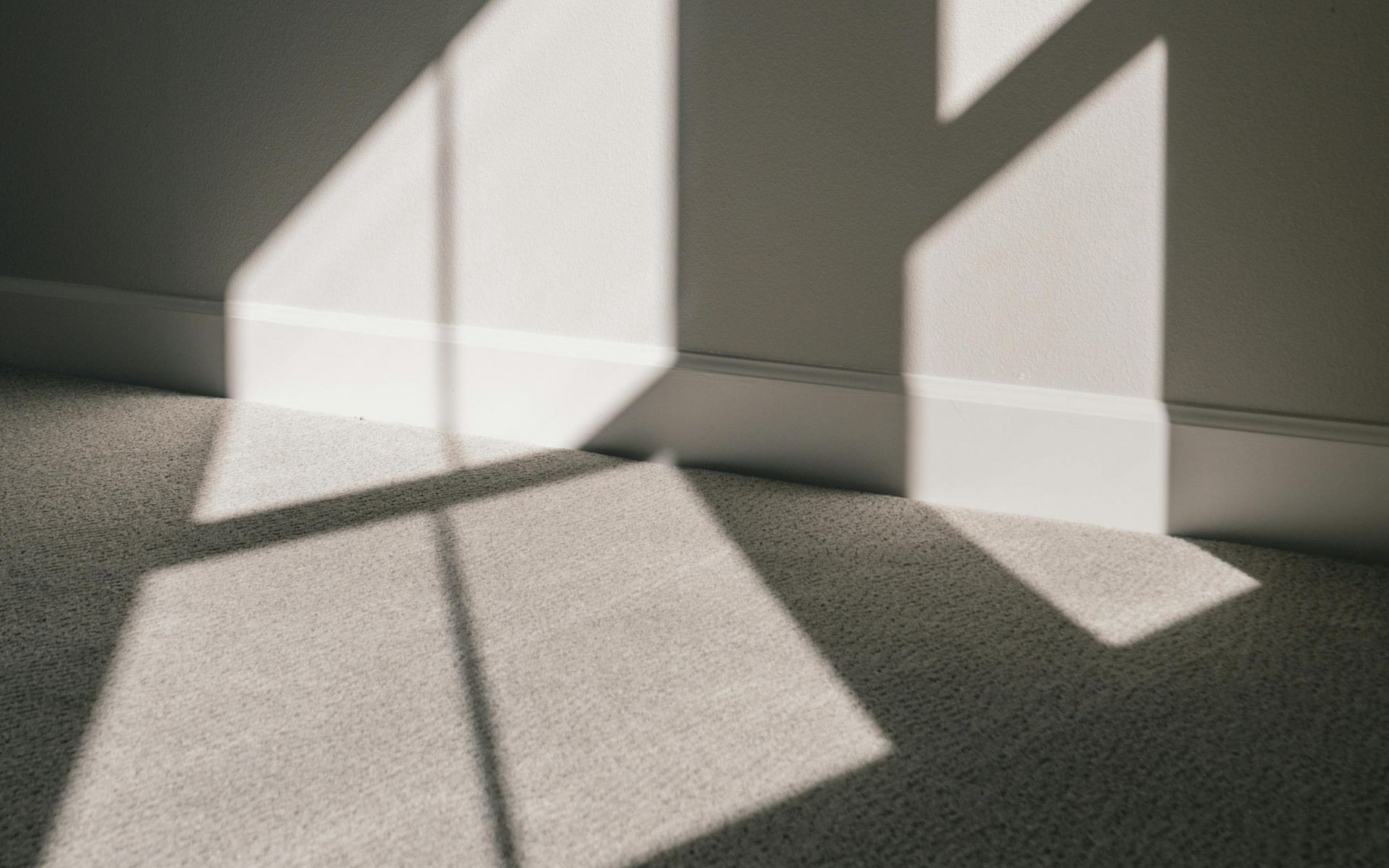 Shadow of a window on a light-colored carpet and wall. Sunlight creating geometric shapes.