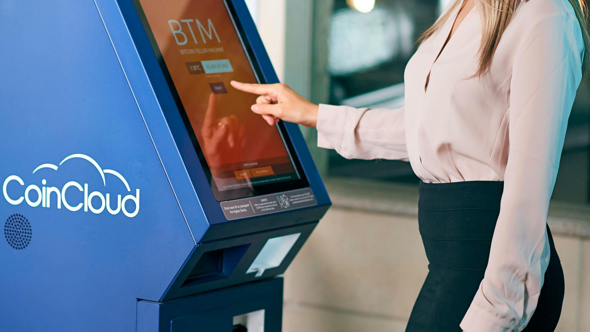 Woman using a CoinCloud Bitcoin ATM; blue machine, pink shirt, touchscreen.