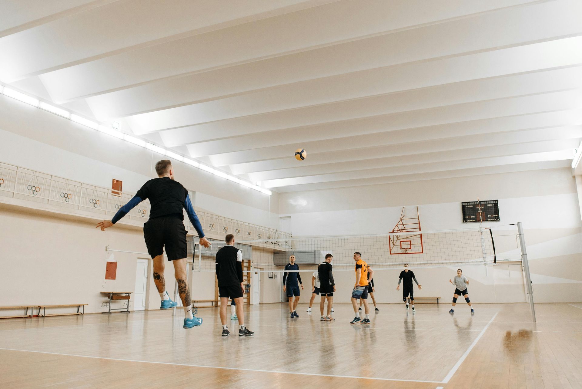Volleyball player jumping to spike ball during a game in a gymnasium.