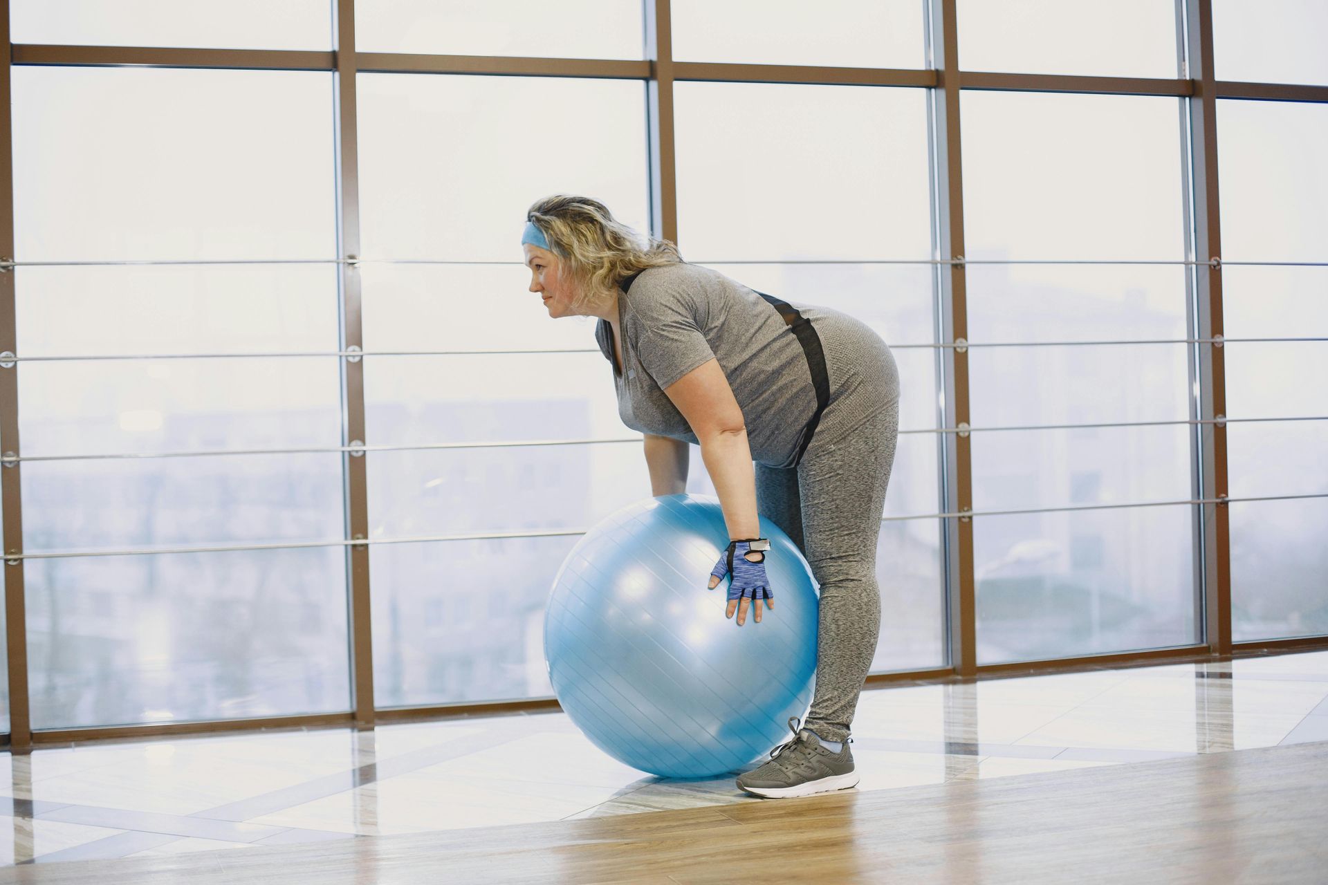 Woman in workout clothes bending over a blue exercise ball in a gym.