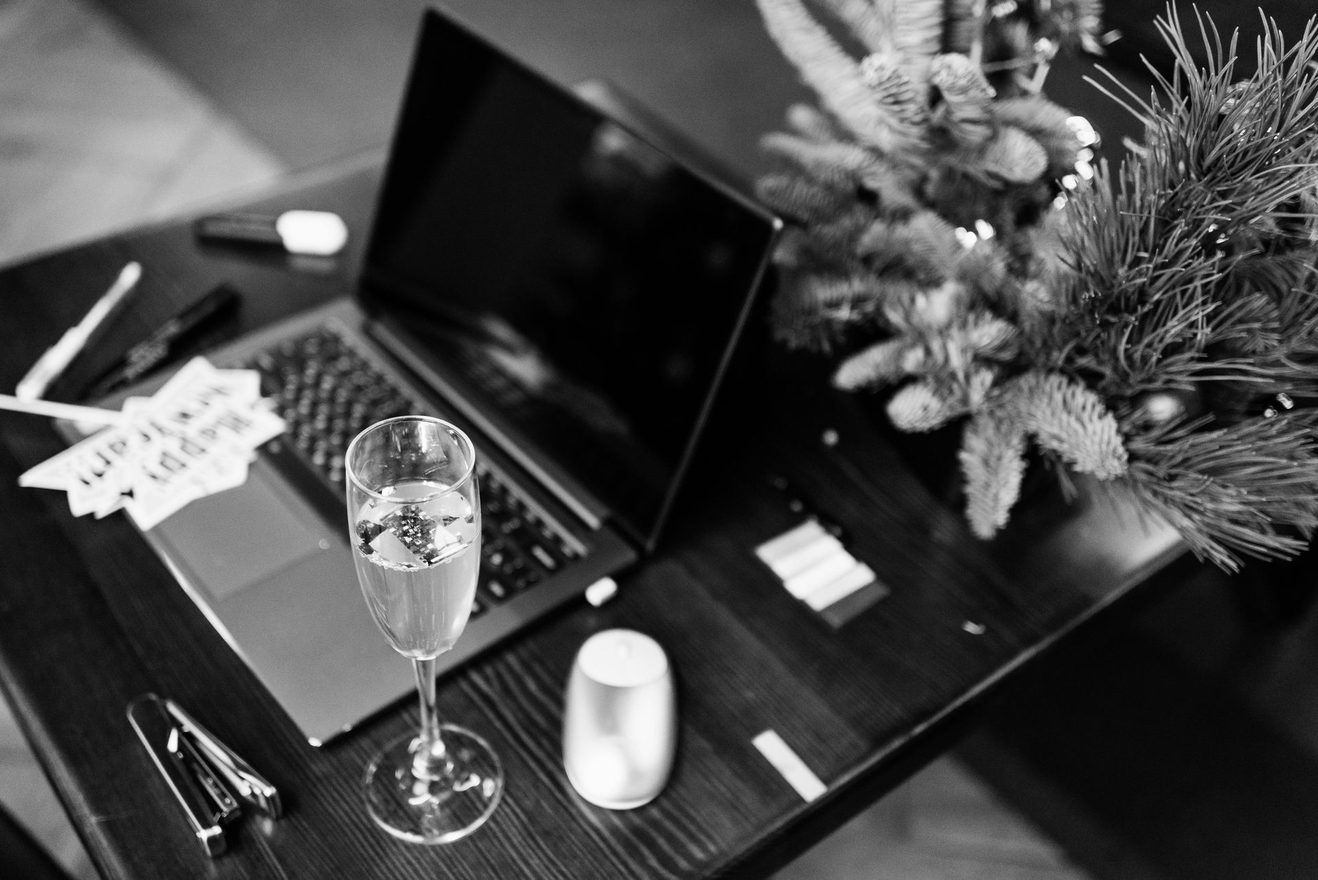 Laptop, champagne glass, and festive decorations on a table, in black and white.