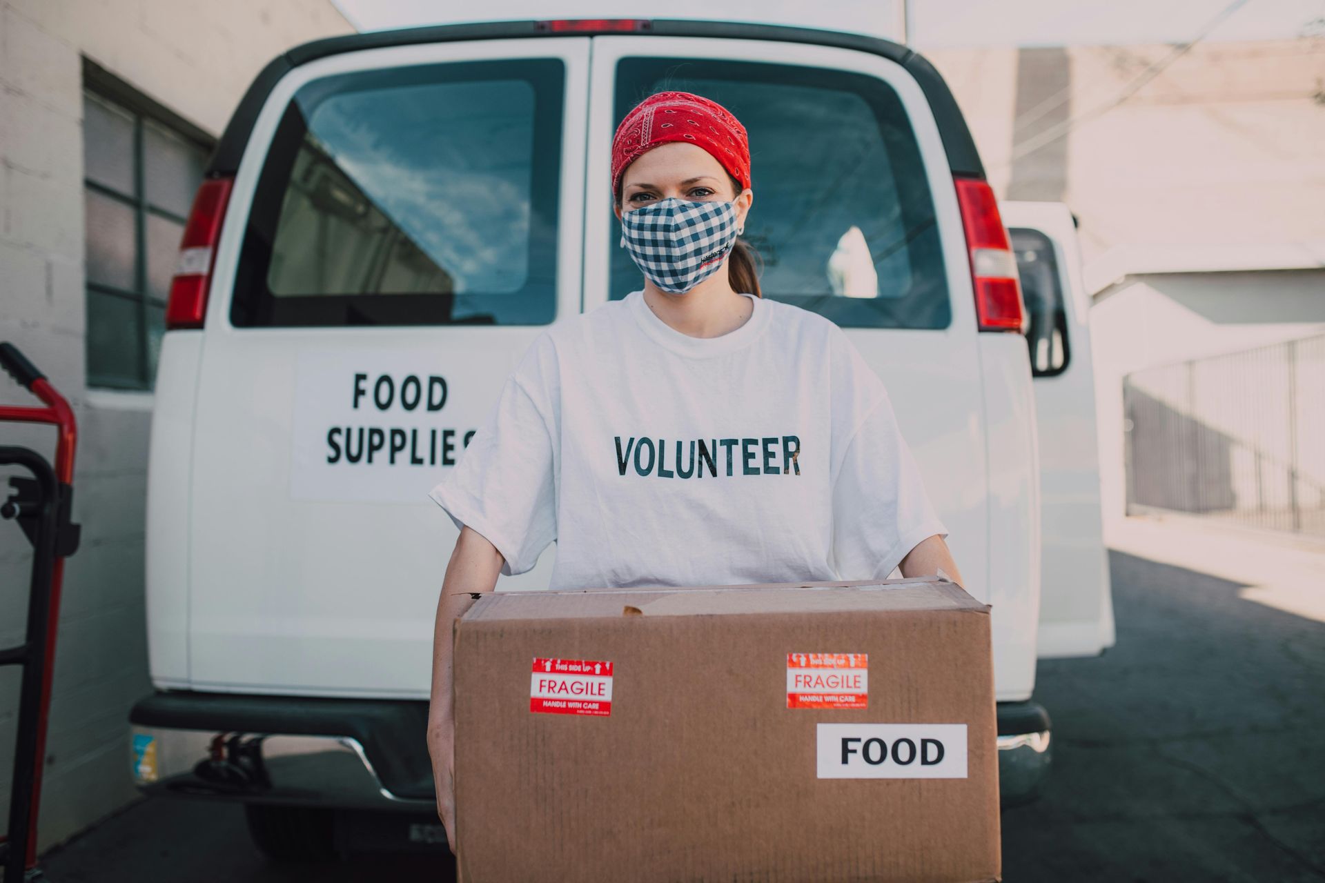 Volunteer carrying a box of food in front of a van labeled