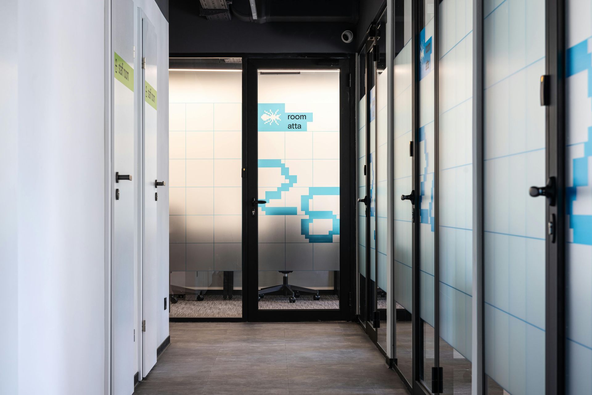 Hallway with frosted glass doors, white walls, and a room with blue pixelated art.