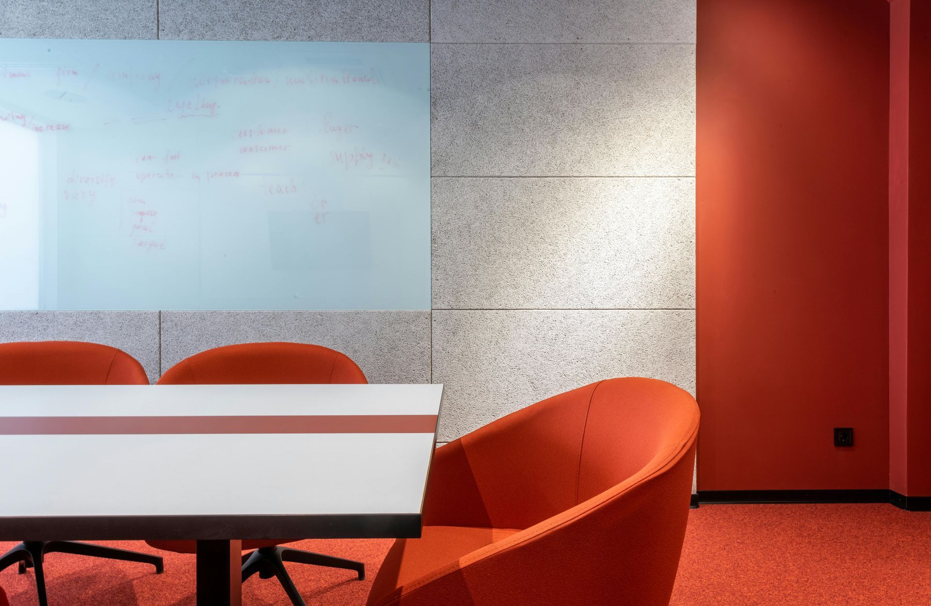 Conference room with white table, orange chairs, whiteboard on speckled wall, and red walls.