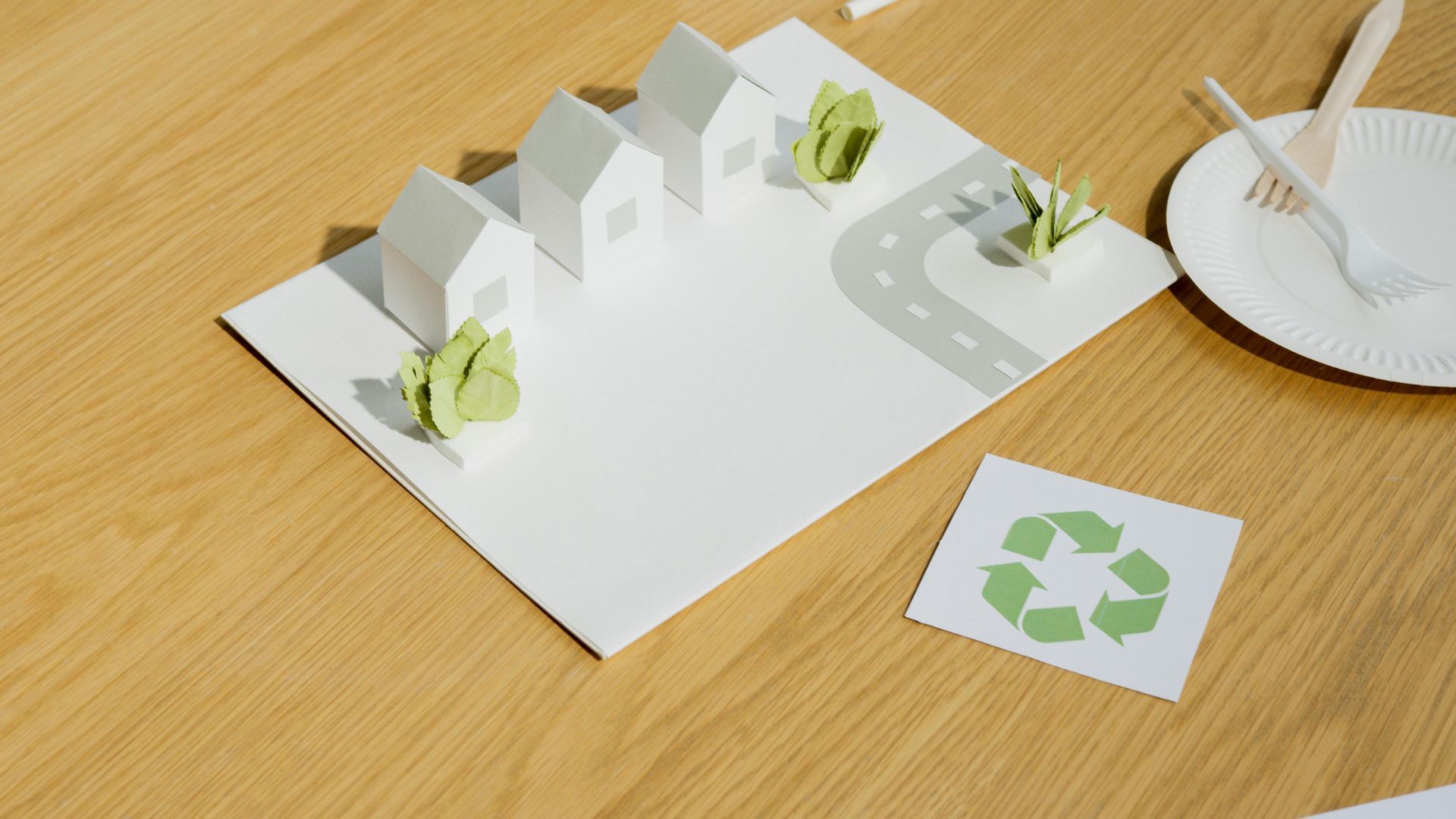 Model of a sustainable town with paper houses, trees, and a recycling symbol.