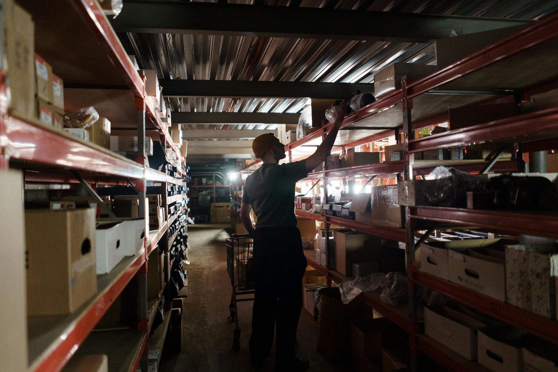 Person reaching for items on a high shelf in a cluttered warehouse.