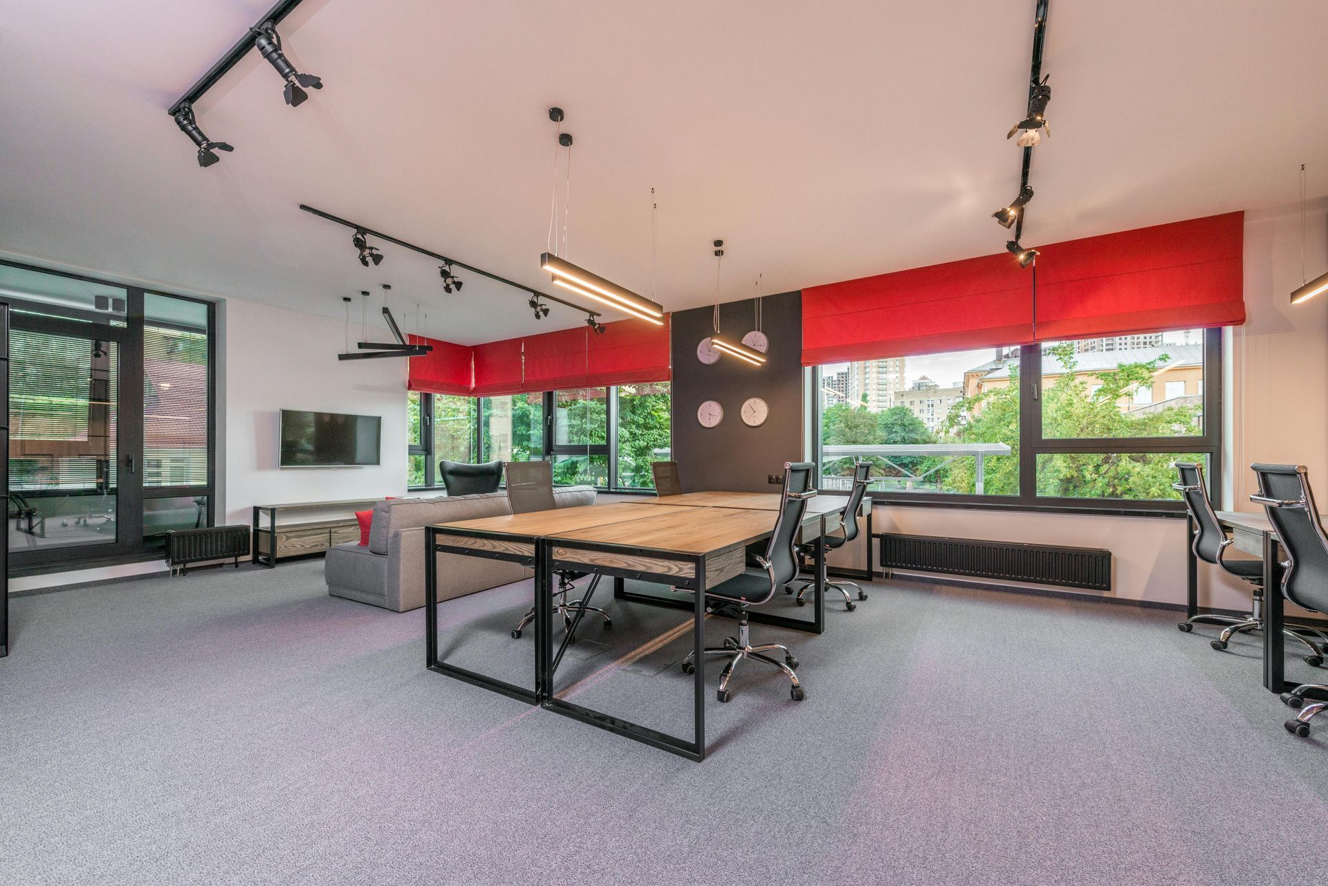 Modern office space with a large table, red accents, and large windows overlooking greenery.