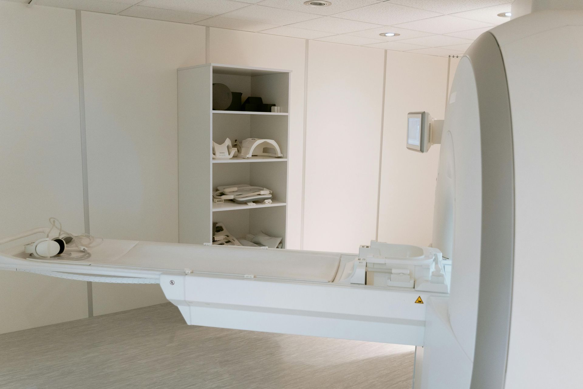 MRI machine with a patient bed, next to a white storage cabinet in a white room.