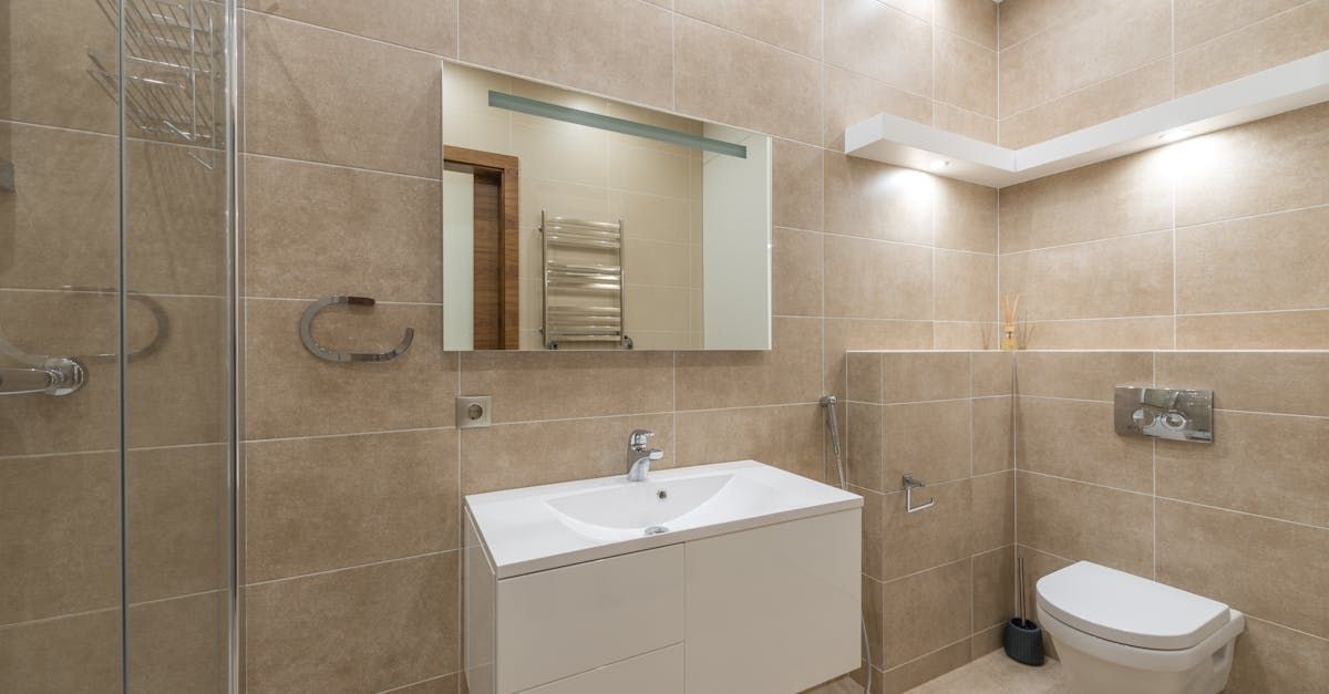 Modern bathroom with beige tile, white vanity, shower, toilet, and large mirror.