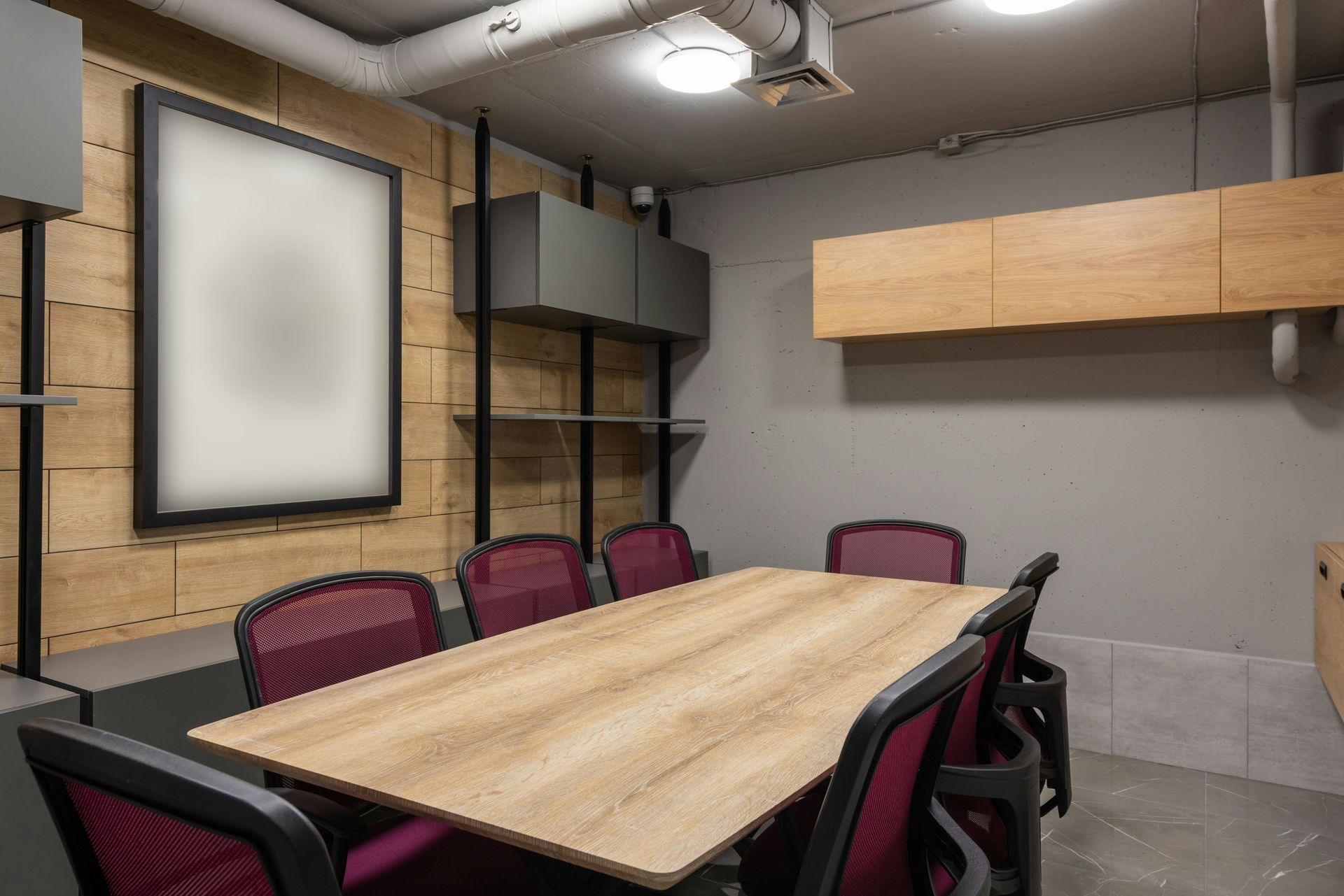 Conference room with wood table, burgundy chairs, and a large blank poster on a wood-paneled wall.