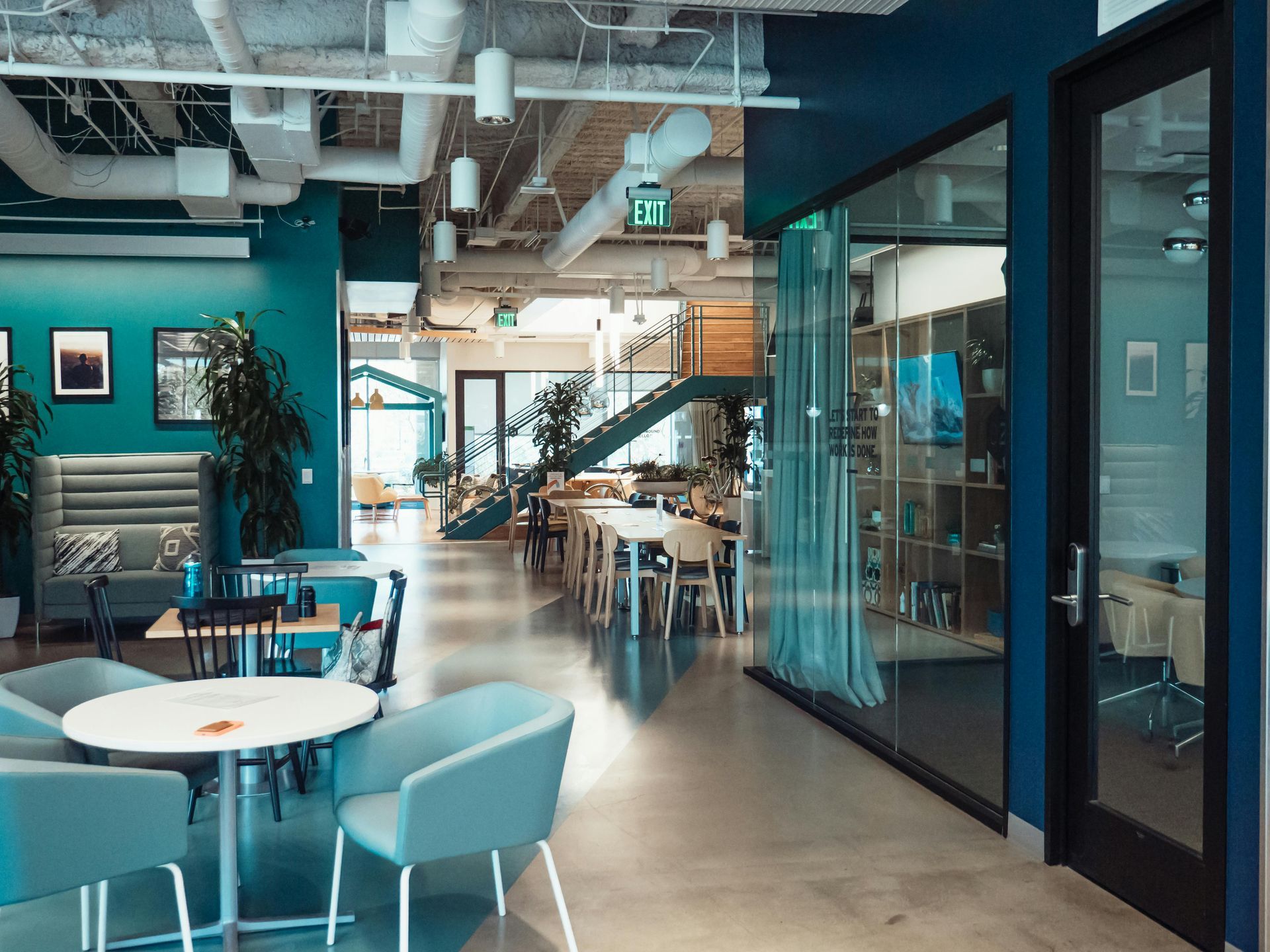 Modern office interior with teal walls, tables, chairs, and a staircase.