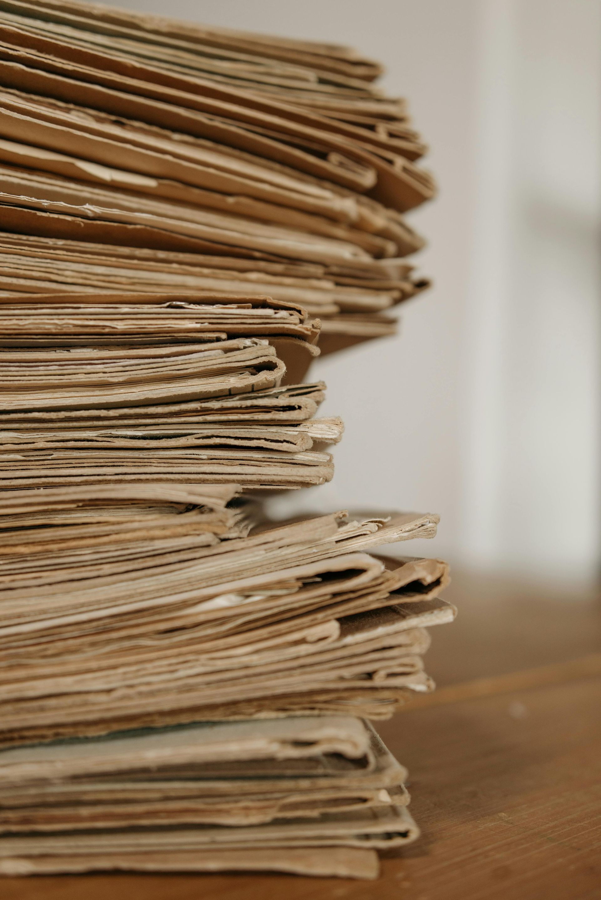 Stack of old, yellowed papers with rough edges, on a wooden surface, neutral background.