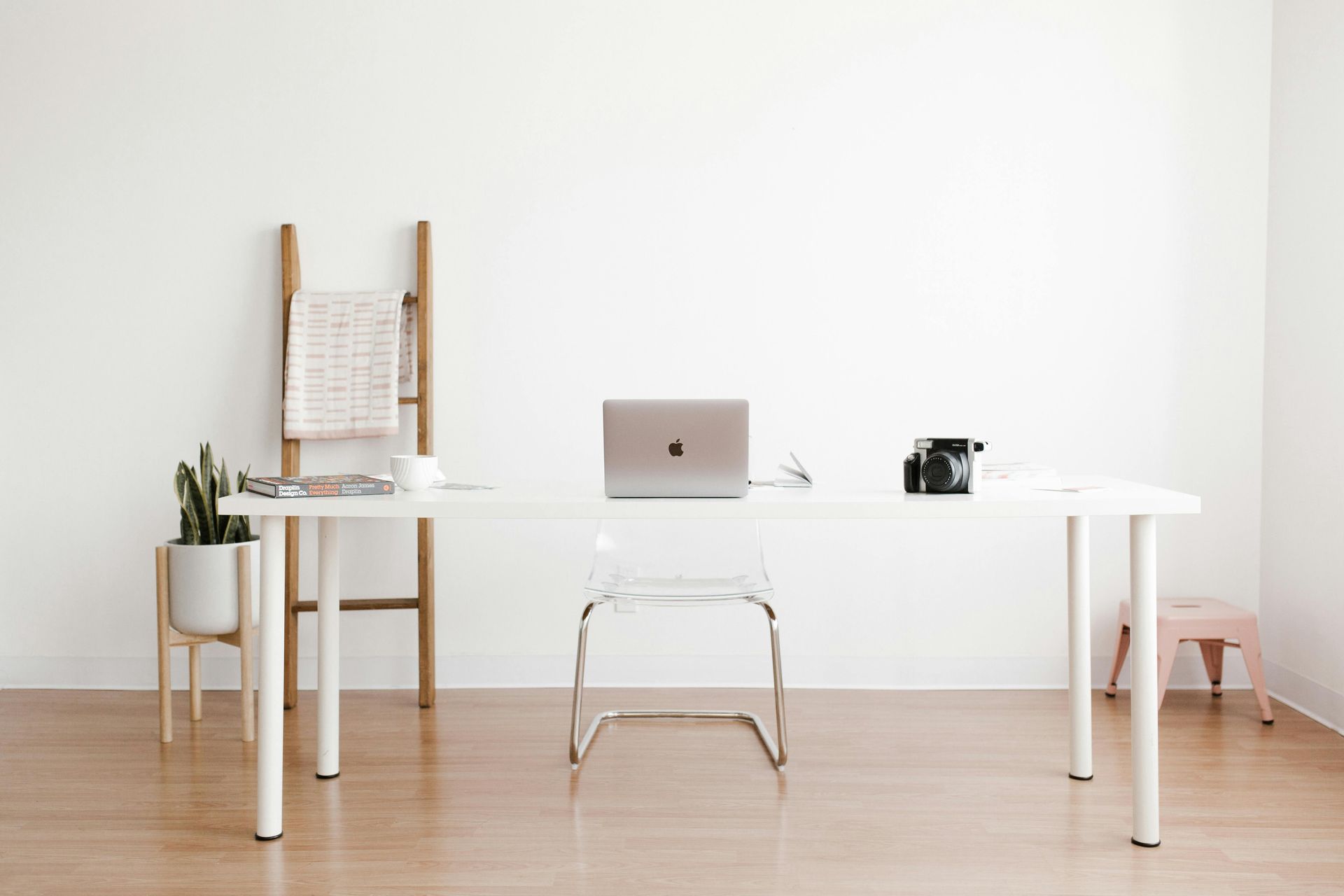Minimalist white home office with laptop, camera, and plant on a desk.