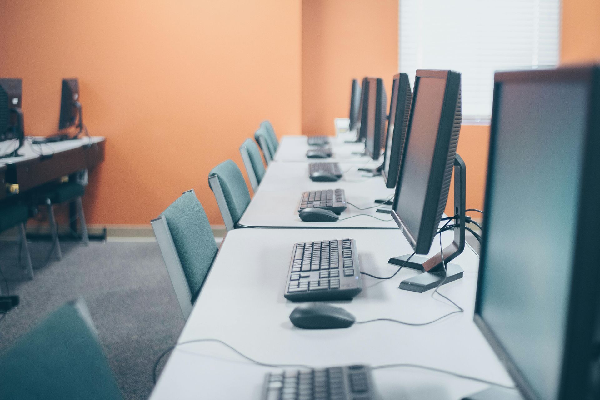 Computer lab with rows of monitors, keyboards, and mice on white desks against an orange wall.