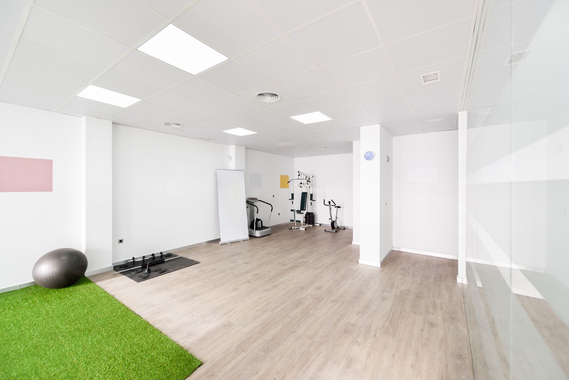 Gym interior with exercise equipment, artificial grass, and light wooden floors.