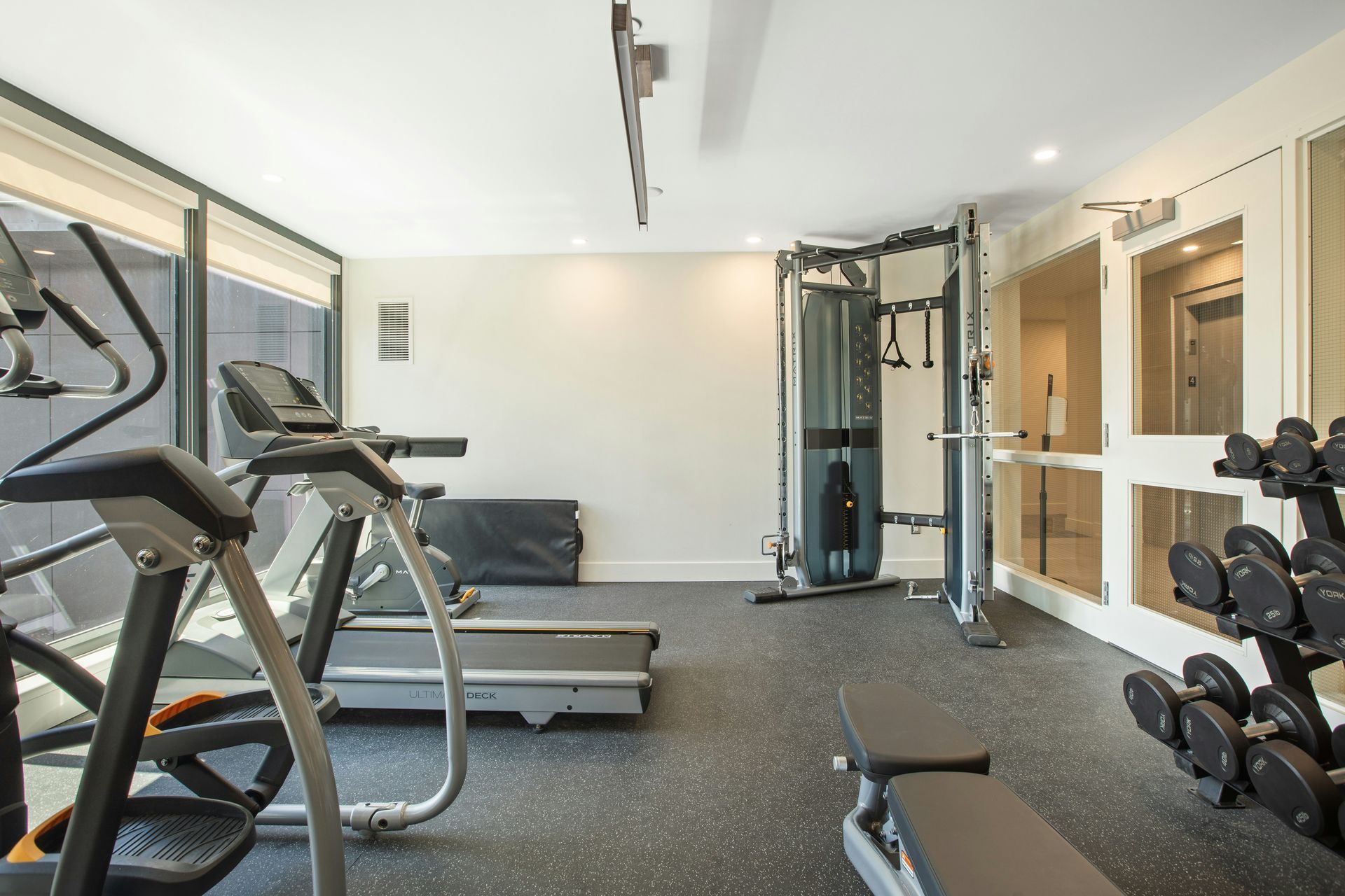 Gym with treadmill, weight machines, free weights, and a weight bench.